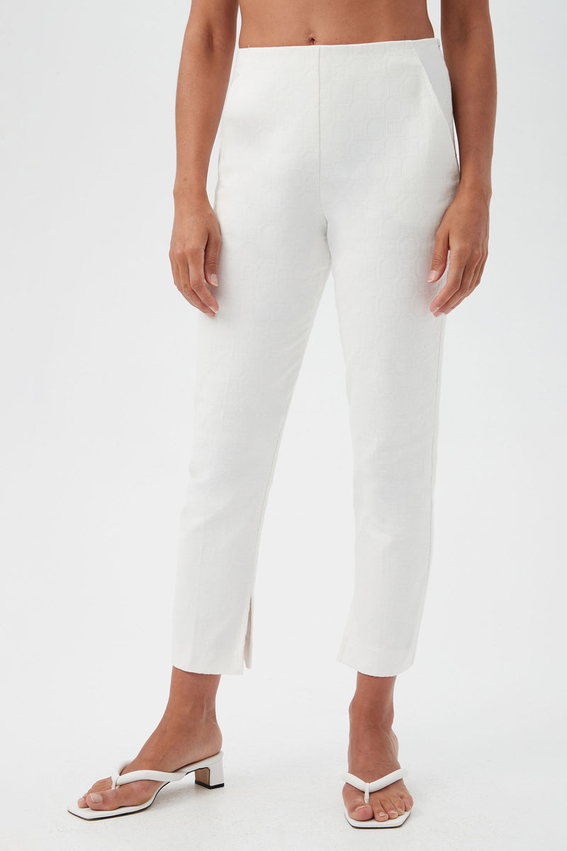 A person wears the Pop Slim-Leg Stretch Pants—high-waisted, white, textured ankle-length with small front slits—paired with white open-toe sandals against a plain white background.