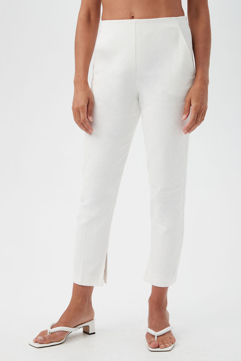 A person wearing Pop Slim-Leg Stretch Pants in Whitewash with a subtle pattern, high waist, slim fit, and small front ankle slits, paired with white heeled sandals. The background is plain white.