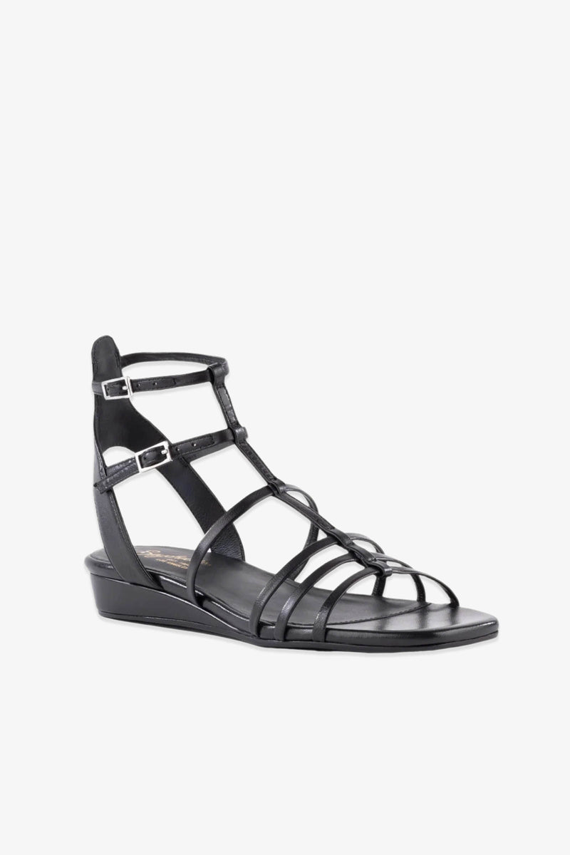 The Luxurious Wedge Sandal - Black Leather features a strappy gladiator design with a low wedge heel, open toe, and two silver buckle ankle straps, displayed against a plain white background.