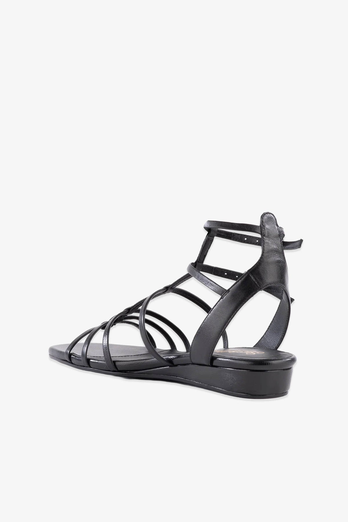 The Luxurious Wedge Sandal in black leather features a strappy flat design with a slight heel, an open toe, and multiple thin straps crossing over the foot and wrapping around the ankle, shown against a white background.