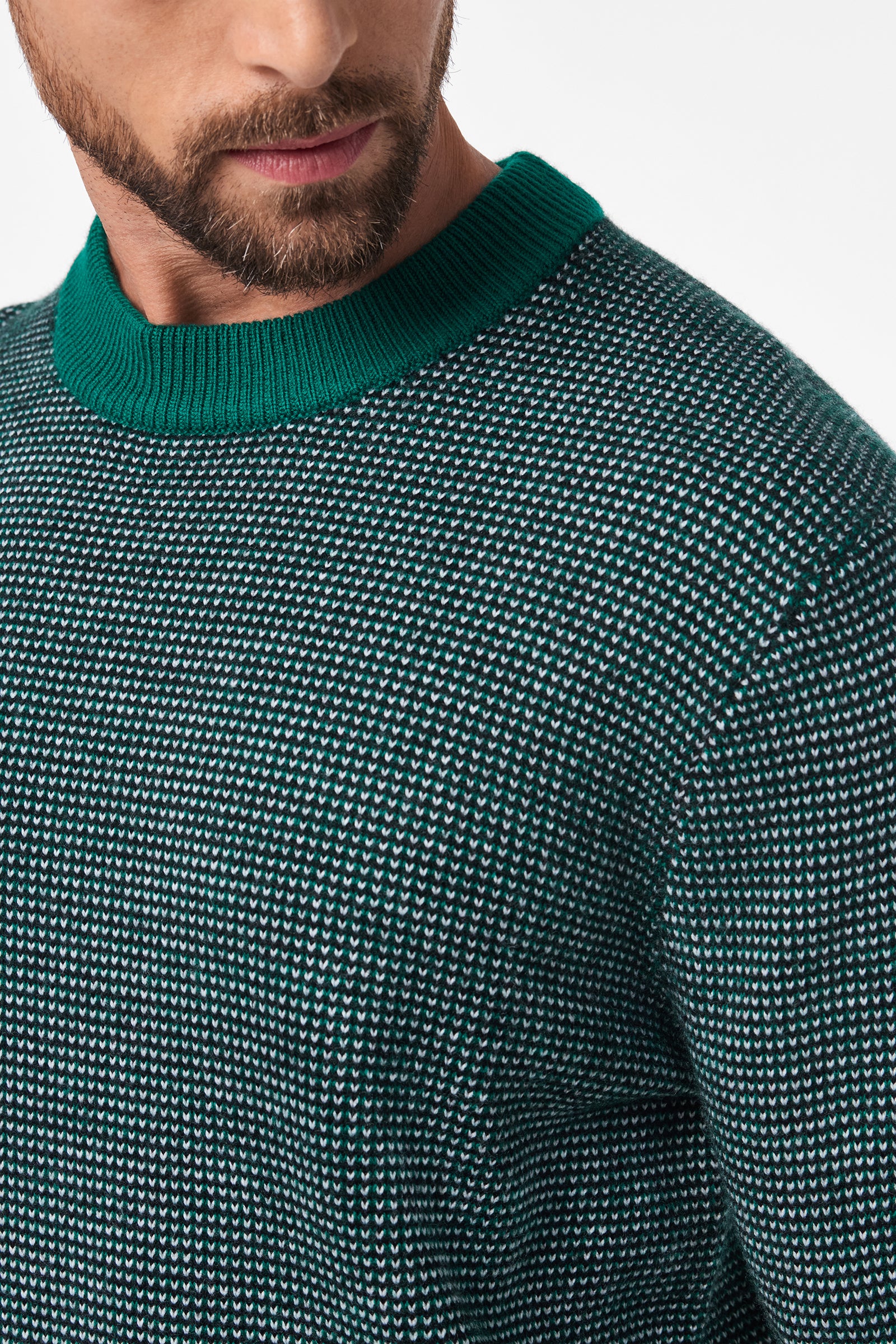 Close-up of a man wearing the Ezra Crewneck, a textured green and white knit sweater featuring a solid green ribbed collar. The image highlights the upper chest, shoulder, and part of his face with beard visible.