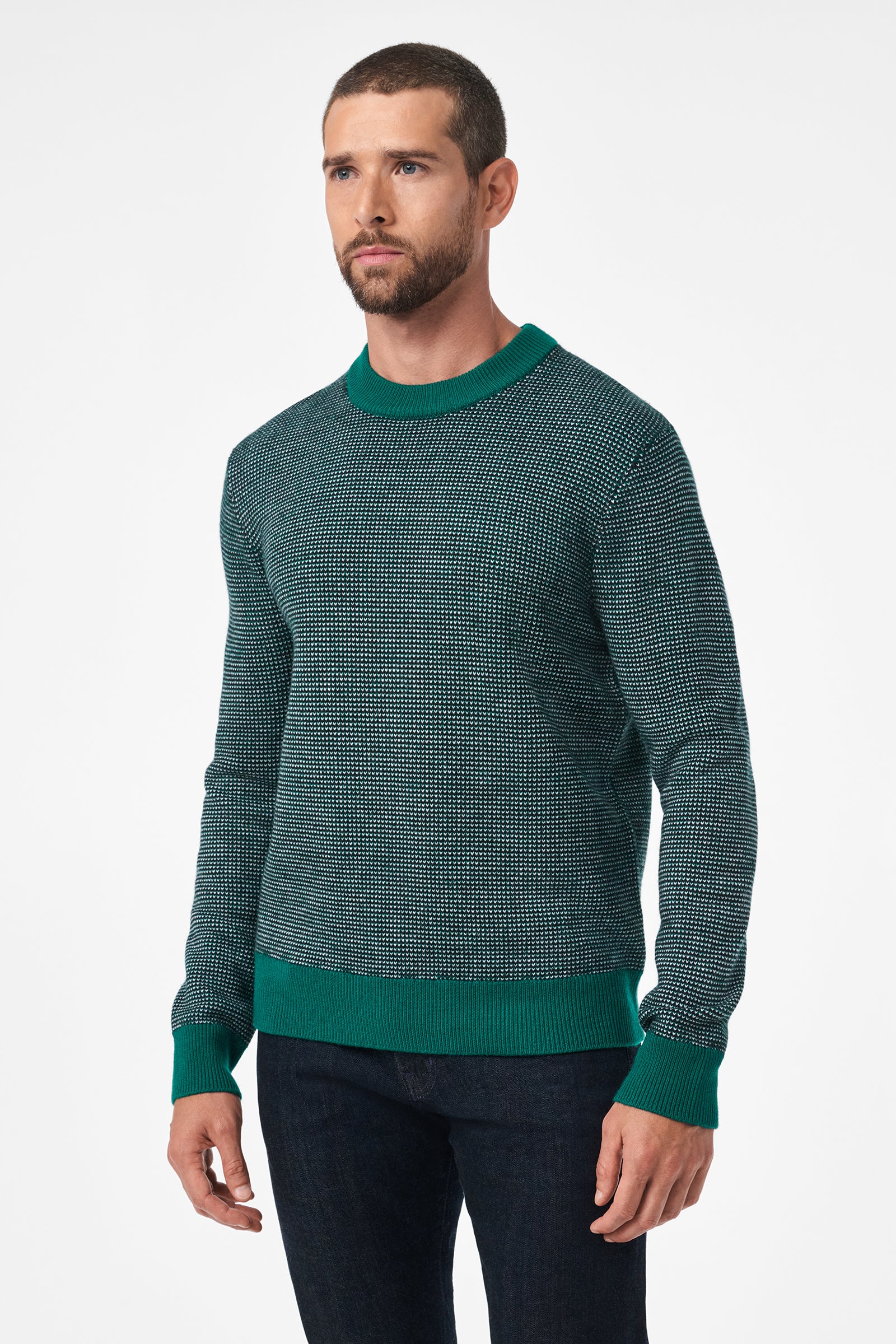 A man with short hair and a beard wears the Ezra Crewneck, a textured green sweater with ribbed cuffs, hem, and collar, paired with dark jeans. He stands against a plain white background.