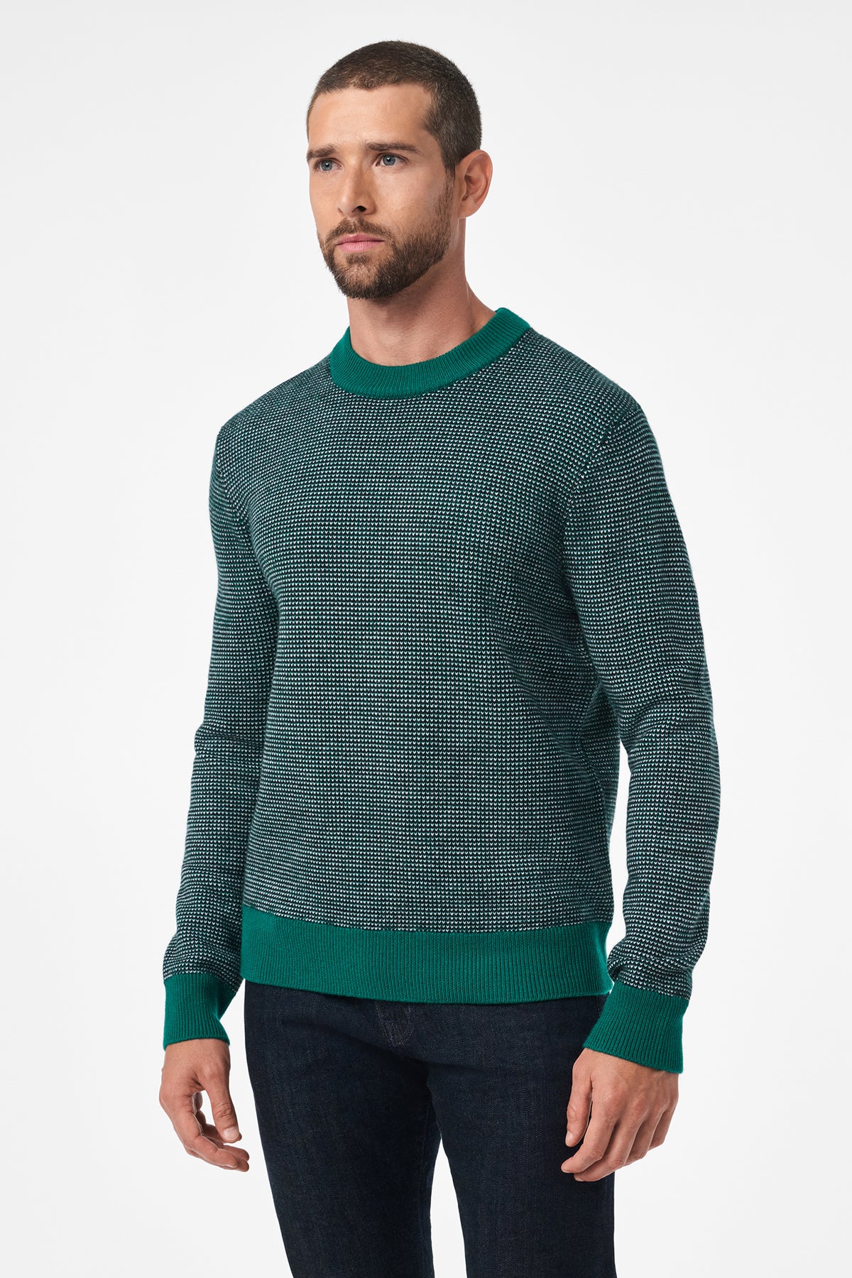 A man with short hair and a beard wears the Ezra Crewneck, a textured green sweater with ribbed cuffs, hem, and collar, paired with dark jeans. He stands against a plain white background.