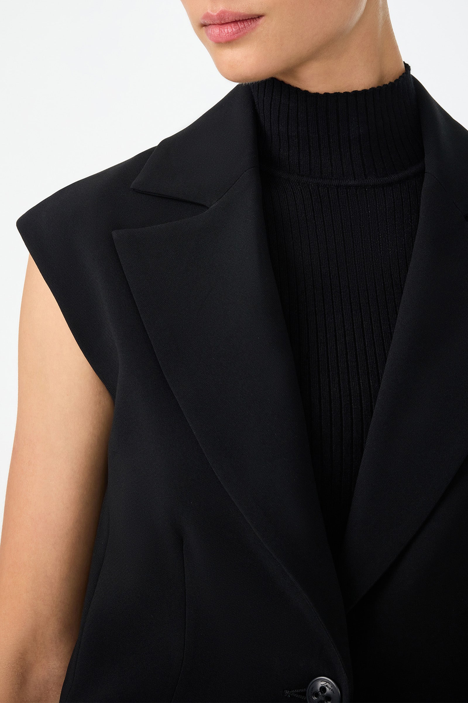 A person models the Boabab Sleeveless Jacket over a ribbed black turtleneck, shown from shoulders to chin against a plain light background.