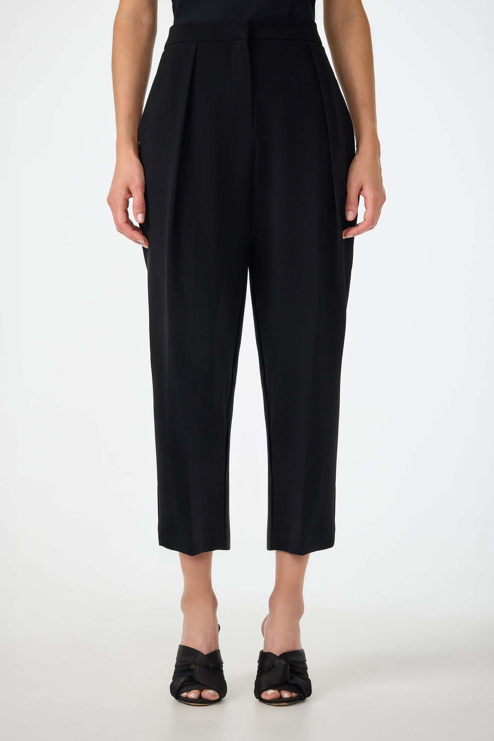 A person wearing Larch Tailored Cropped Pants in black and black heeled sandals stands against a plain white background.