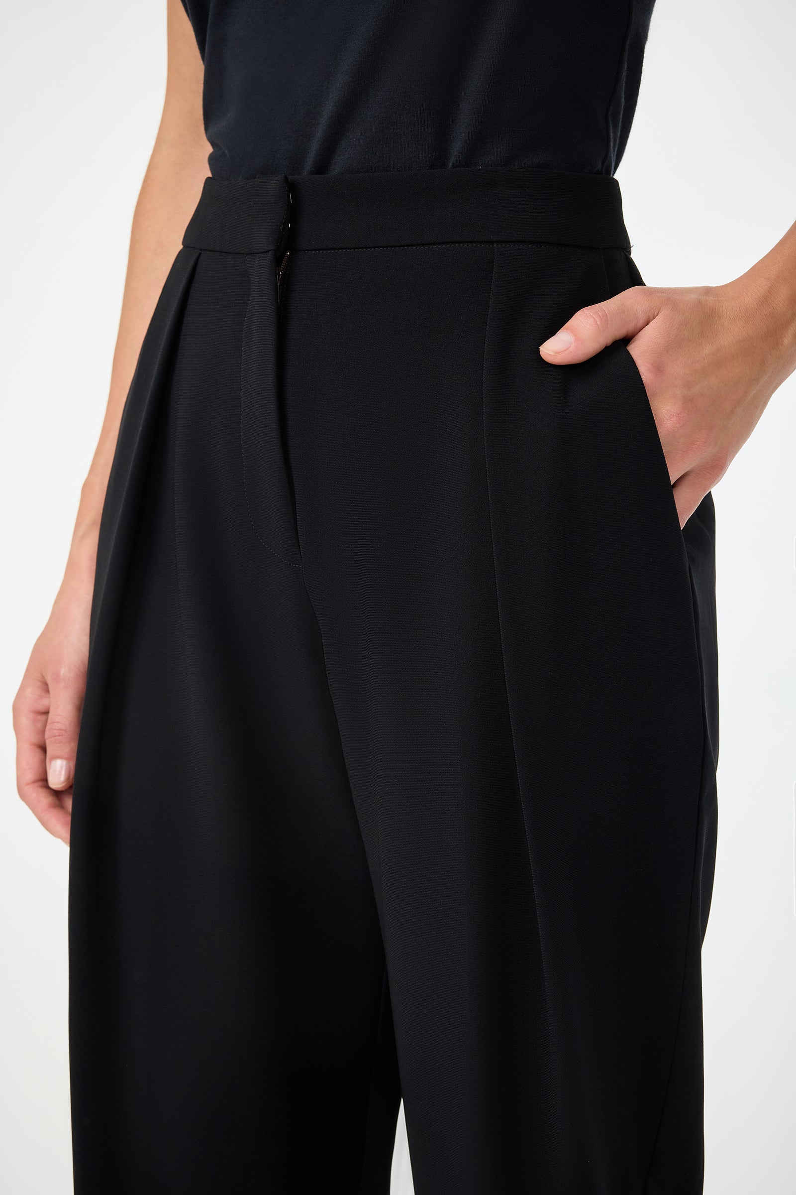 A person wears Larch Tailored Cropped Pants and a black top, standing against a plain background with one hand in their pocket and the other arm relaxed by their side.