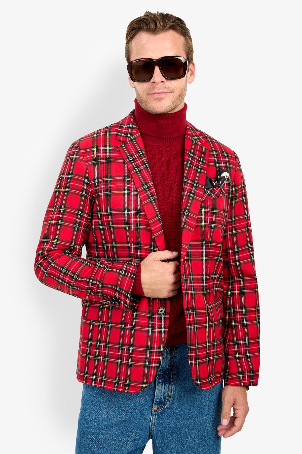 Man wearing large sunglasses, the Thurston Blazer in red plaid over a red turtleneck, and blue jeans, standing against a plain white background.