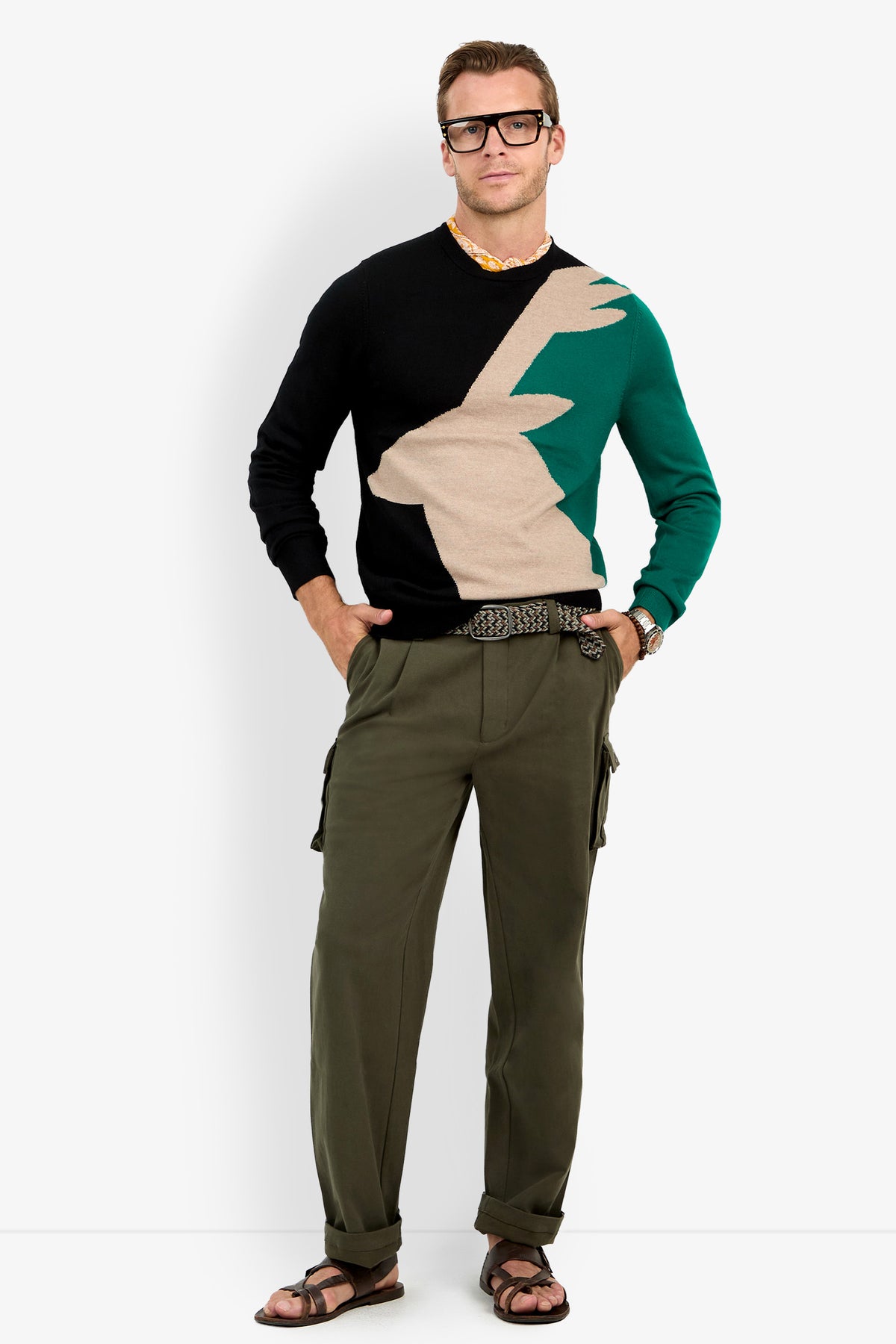 A man in glasses wears a Crewneck Sweater, olive cargo pants, belt, and brown sandals, standing confidently with hands in pockets against a plain white background.