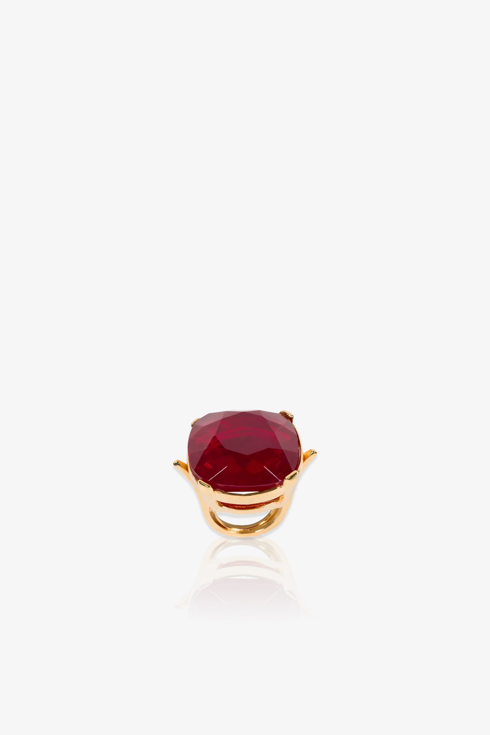 A Ruby Faceted Cocktail Ring featuring a large, faceted deep red gemstone set in a prong setting is displayed on a white background with a subtle reflection beneath it.
