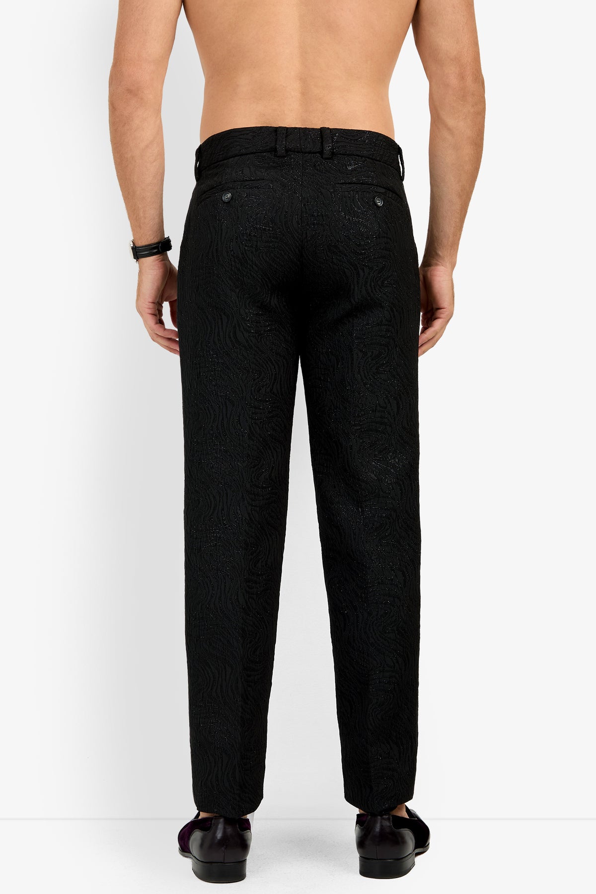 A shirtless person is standing with their back to the camera, wearing the Clyde Slim Trouser in textured black along with black shoes.