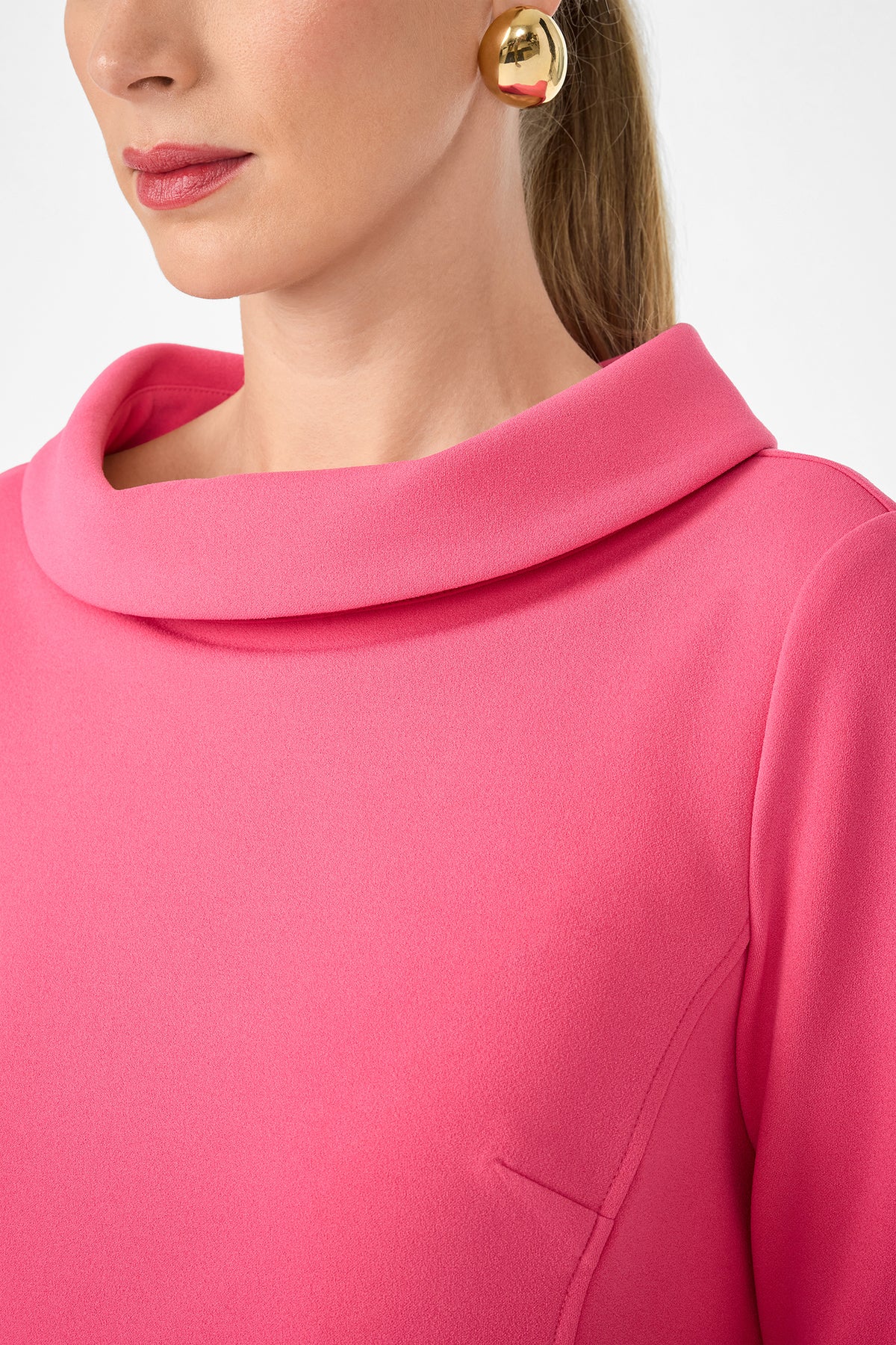 Wearing the Maleko Dress, a woman with her hair tied back and gold round earrings is shown; only the lower half of her face and upper torso are visible.