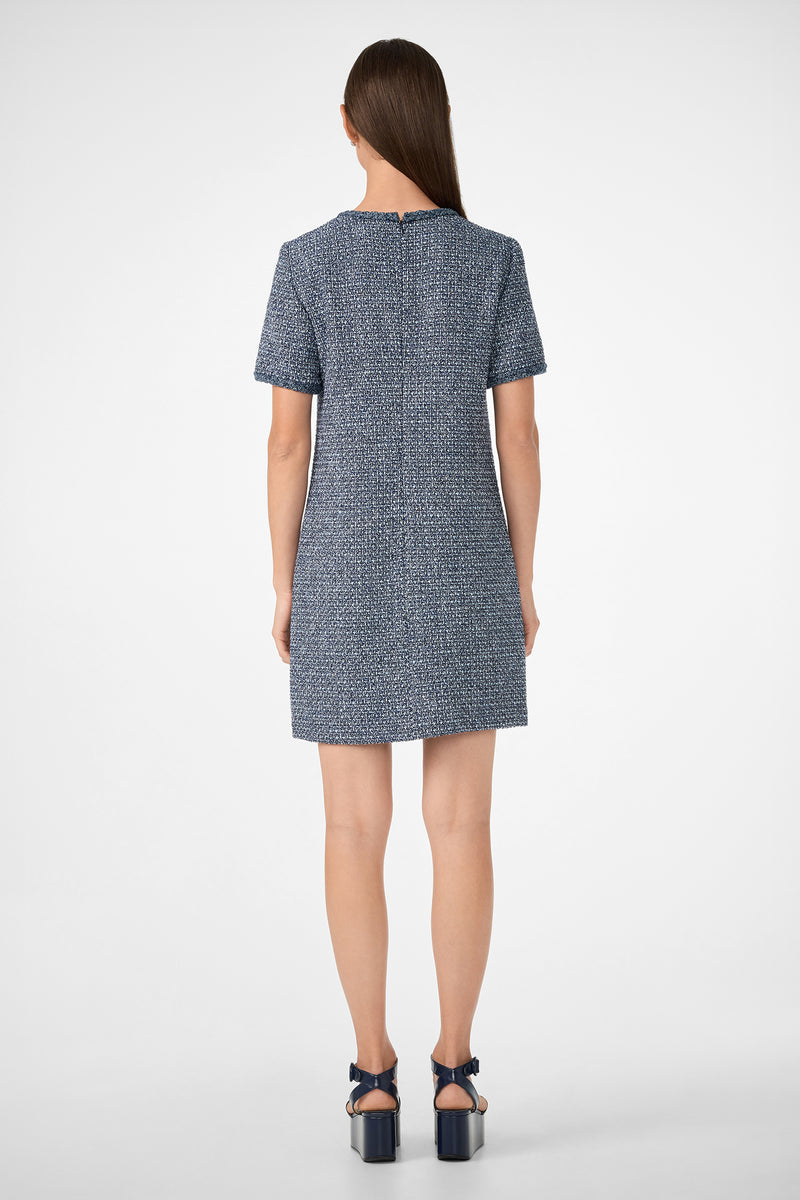 A woman with straight brown hair, seen from behind, wears the Akara Dress—a short-sleeve, textured blue dress—with dark blue platform sandals against a plain white background.
