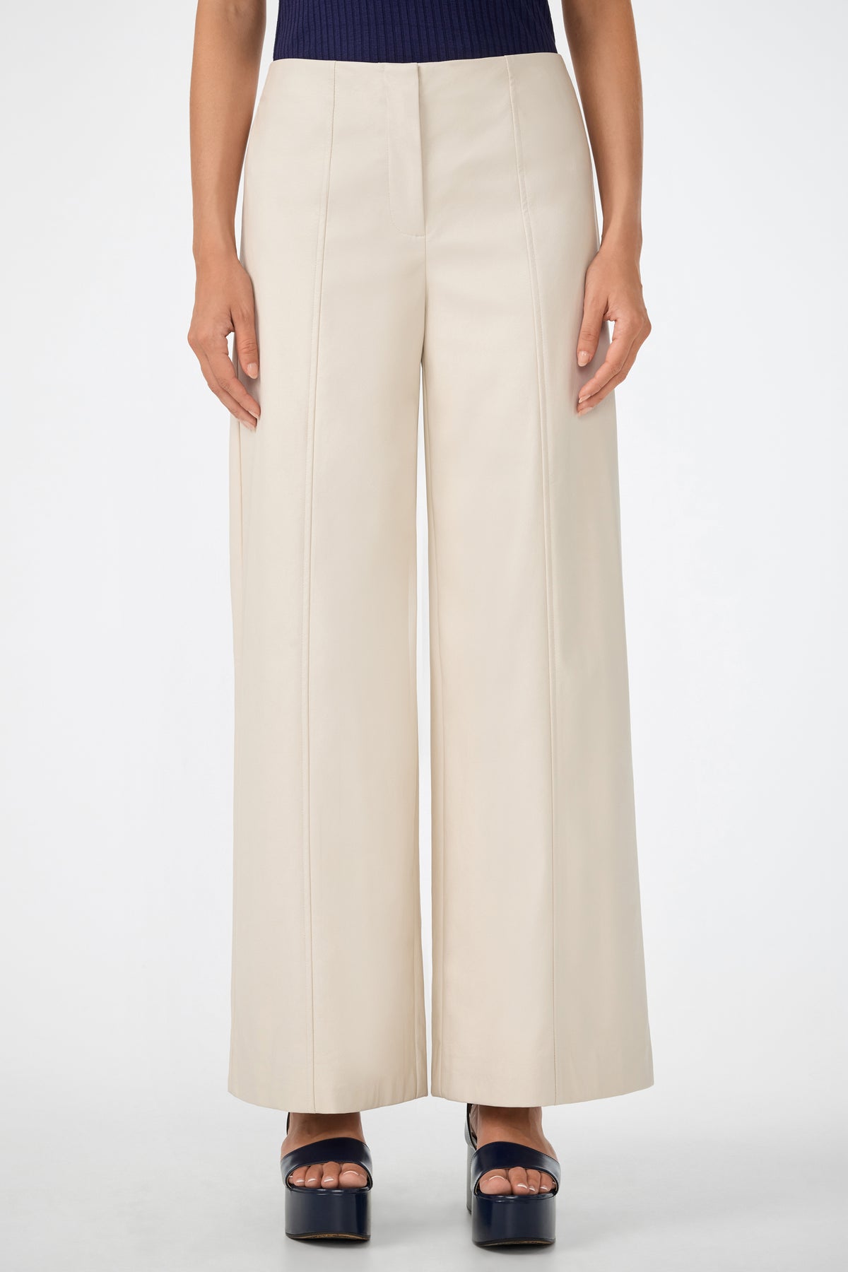 A person models the Parque Pant, a high-waisted, wide-leg cream-colored style. Only their lower torso and legs are shown as they stand against a plain white background in black platform heels.