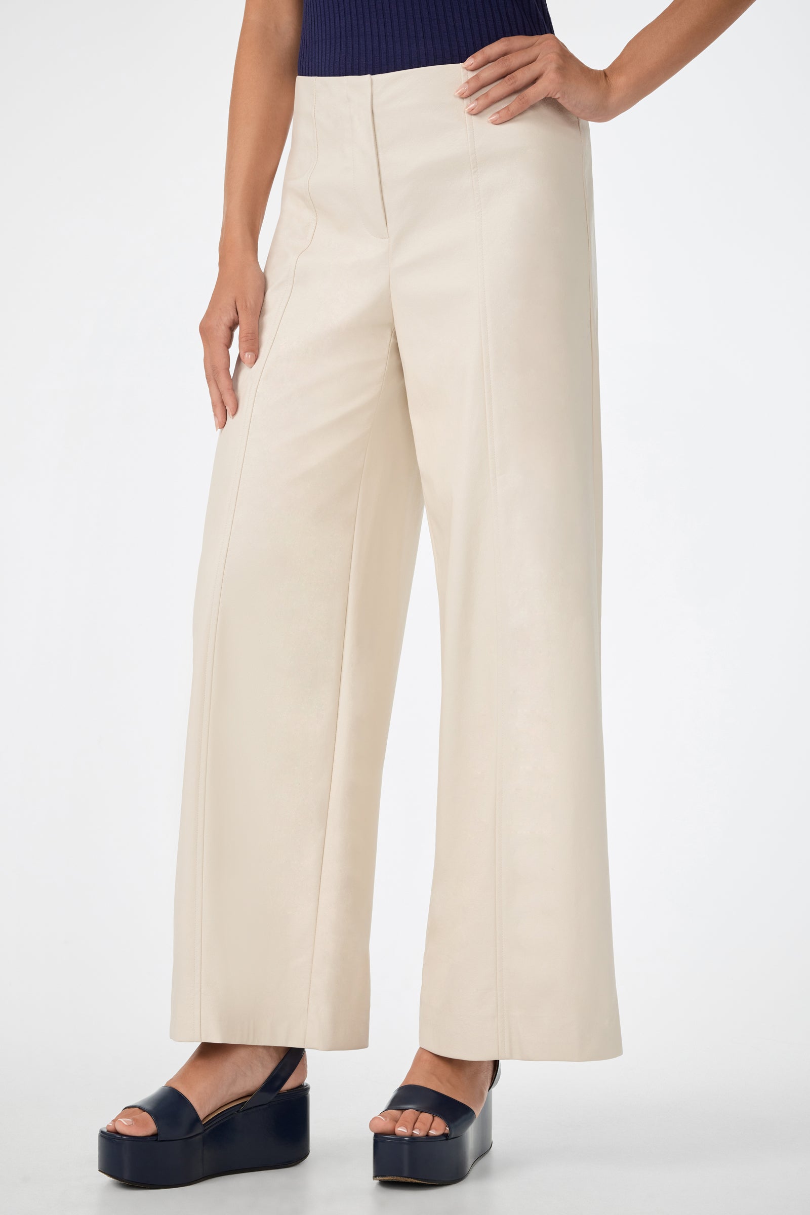 A person wearing the Parque Pant—wide-leg, high-waisted cream pants—with navy platform sandals, one hand on their hip, stands against a plain white background.