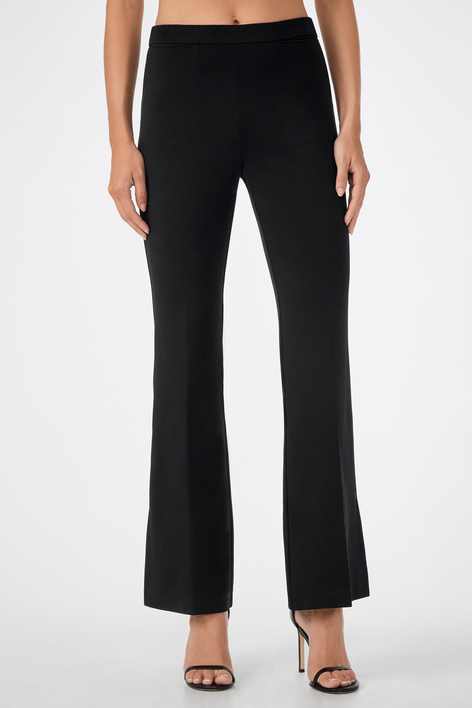 A person wearing the Mona Pant—high-waisted, black, flared pants—and black high-heeled sandals, standing against a plain white background.