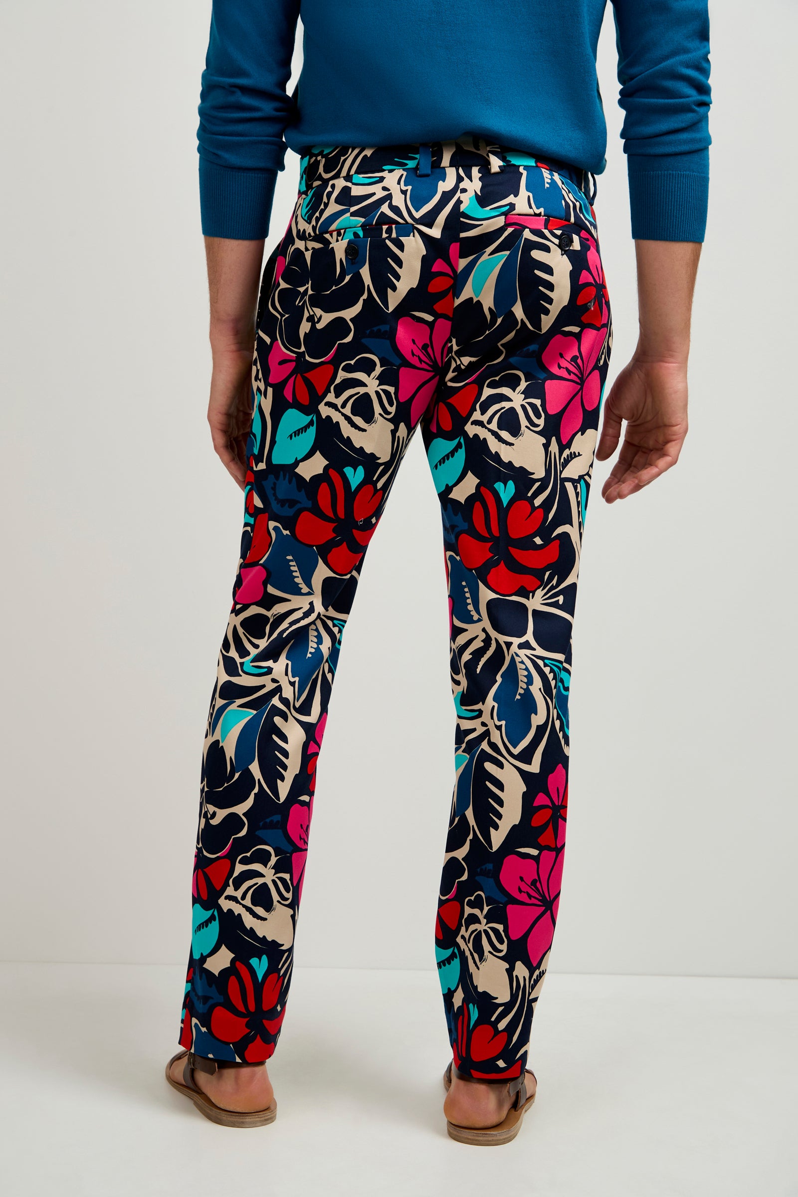 A person wearing Clyde Slim Trouser - Copacabana, a blue sweater, sandals, and a black belt stands with their back to the camera against a plain white background.