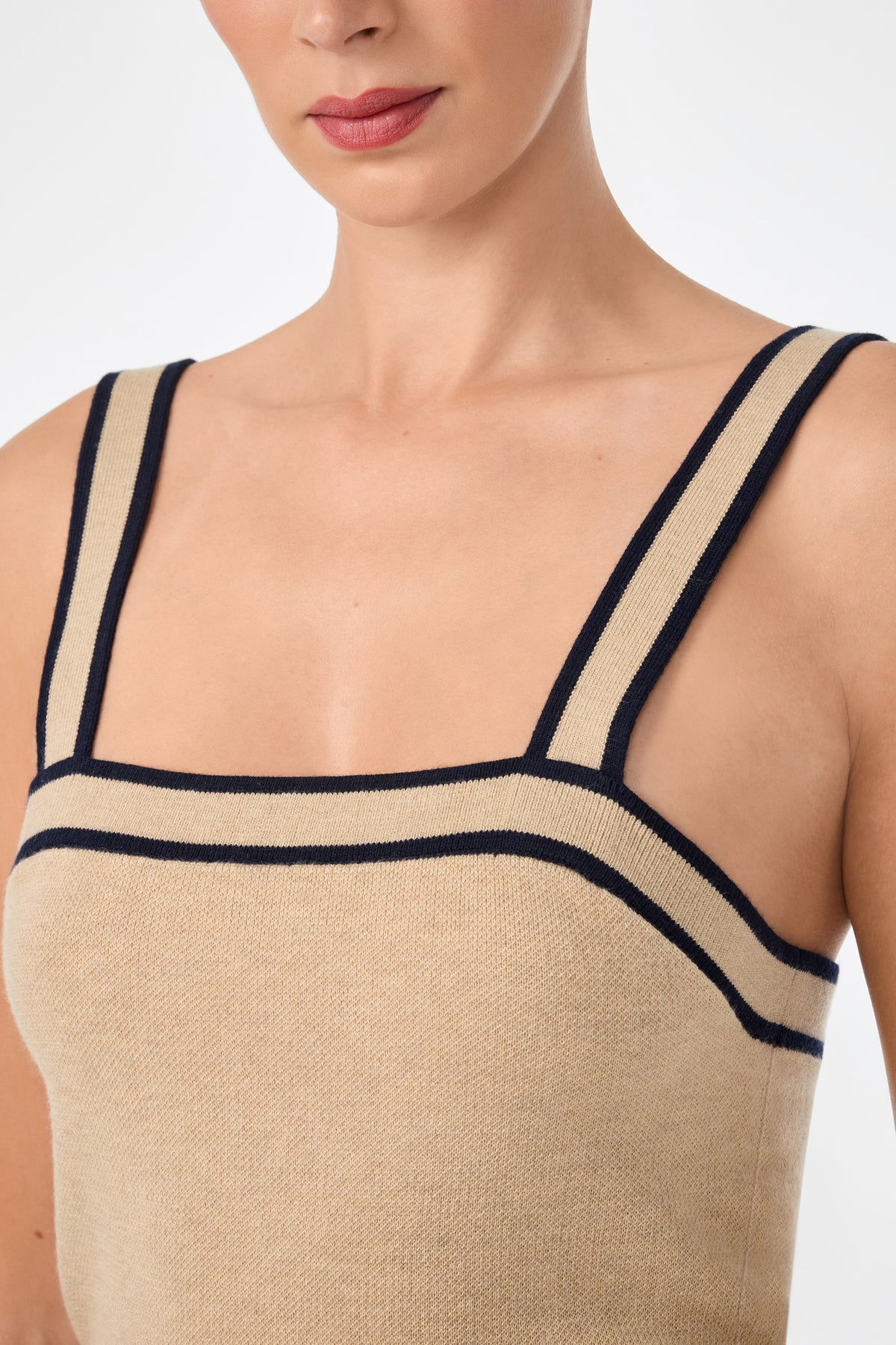 A woman models the Casady Cami, a sleeveless beige top with wide, dark trim on the straps and neckline, shown from shoulders to just above the waist against a plain background.