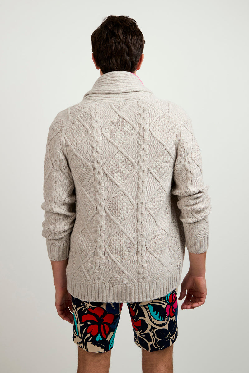 A man stands facing away, wearing the Brighton Cardigan—a light gray, patterned knit sweater—and colorful floral shorts against a plain white background.