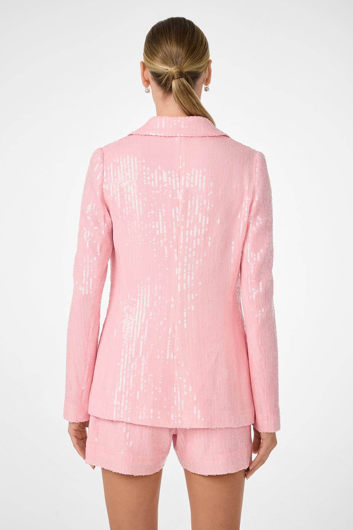 A person with long, straight hair in a low ponytail wears the shiny light pink Alternates 2 Blazer and matching shorts, shown from the back against a plain white background.