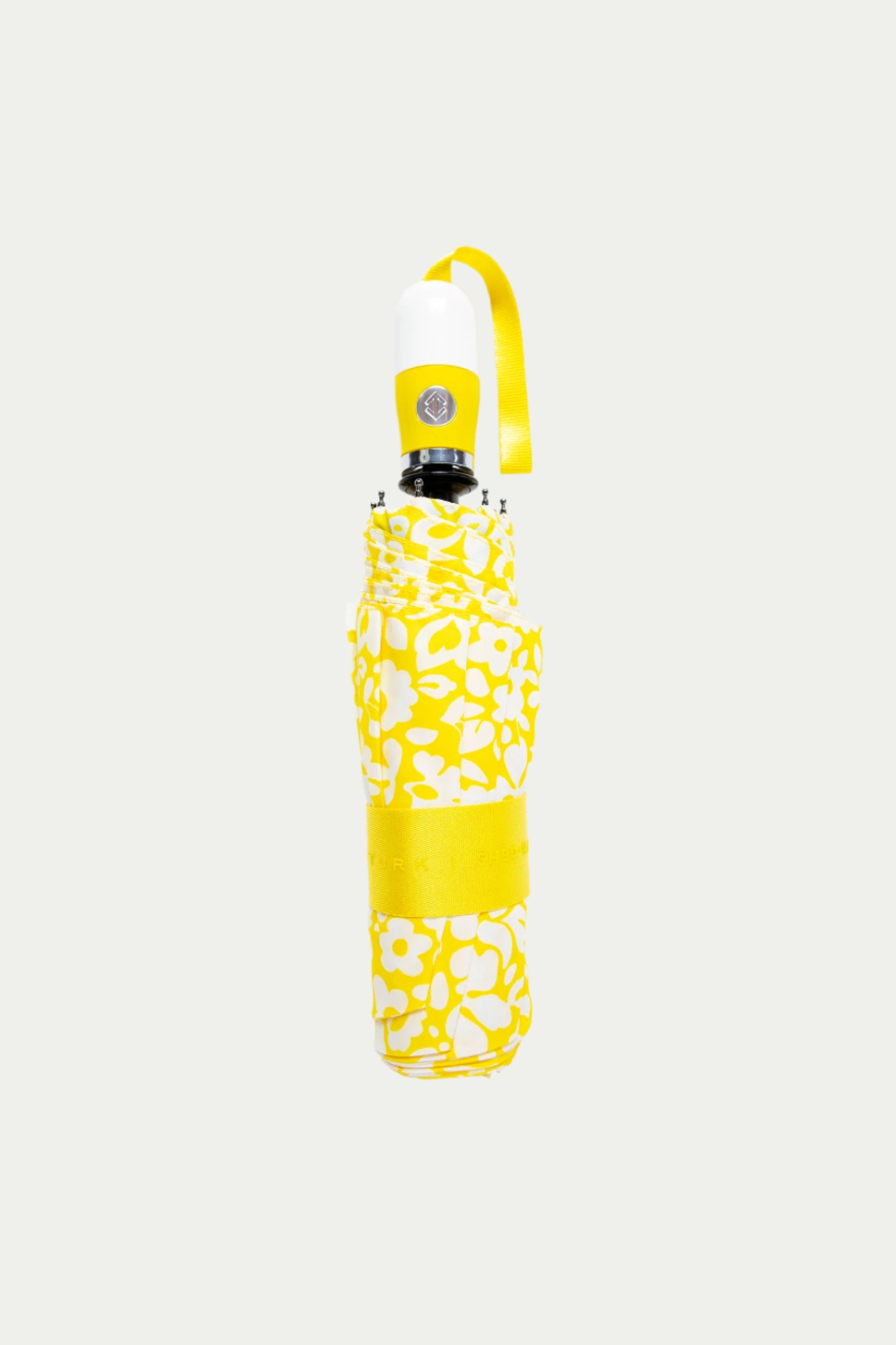 The TT X SR Compact Umbrella - Poolside Gossip features a closed yellow and white floral design with a yellow strap, displayed on a light grey background.