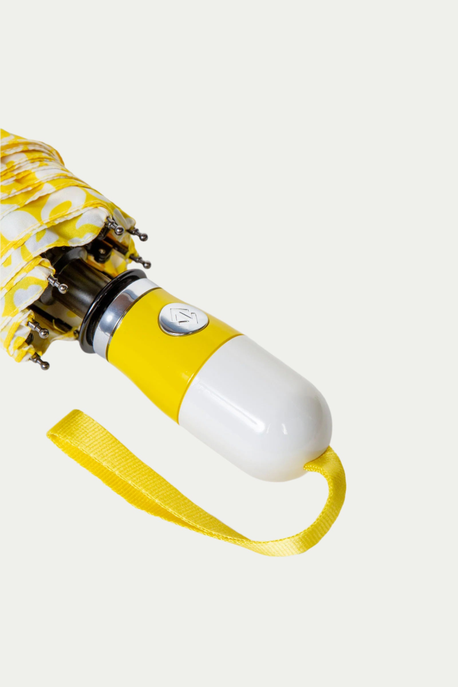 A close-up of the TT X SR Compact Umbrella - Poolside Gossip shows its yellow and white handle, a matching yellow wrist strap, and a folded canopy with a vibrant yellow and white pattern.