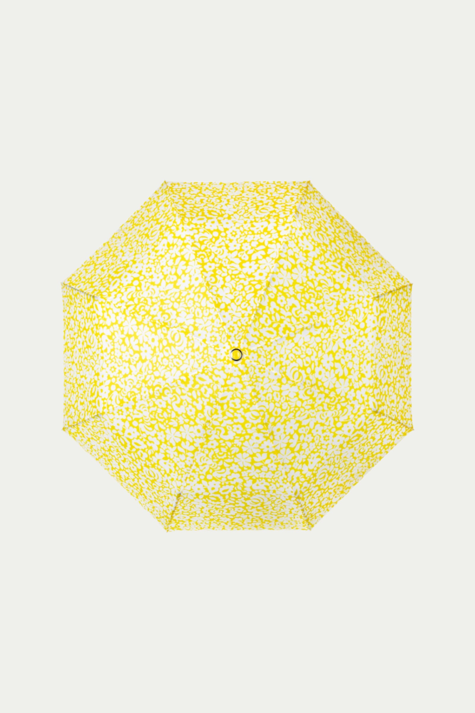 The TT X SR Compact Umbrella - Poolside Gossip is shown from above, displaying a vibrant yellow and white abstract spotted canopy set against a simple light background.