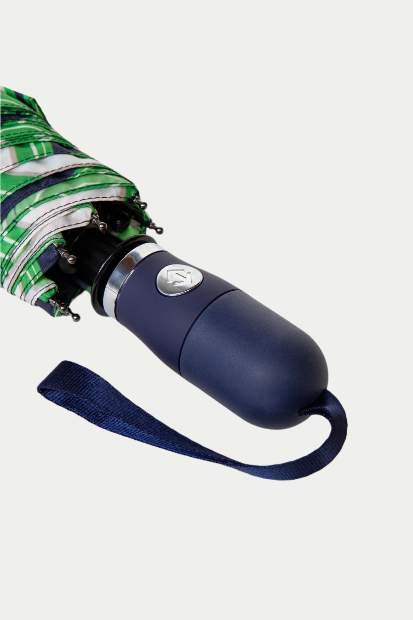 Close-up of the TT X SR Compact Umbrella - Serena Satins navy handle with a silver emblem, blue wrist strap, and green and white striped fabric.