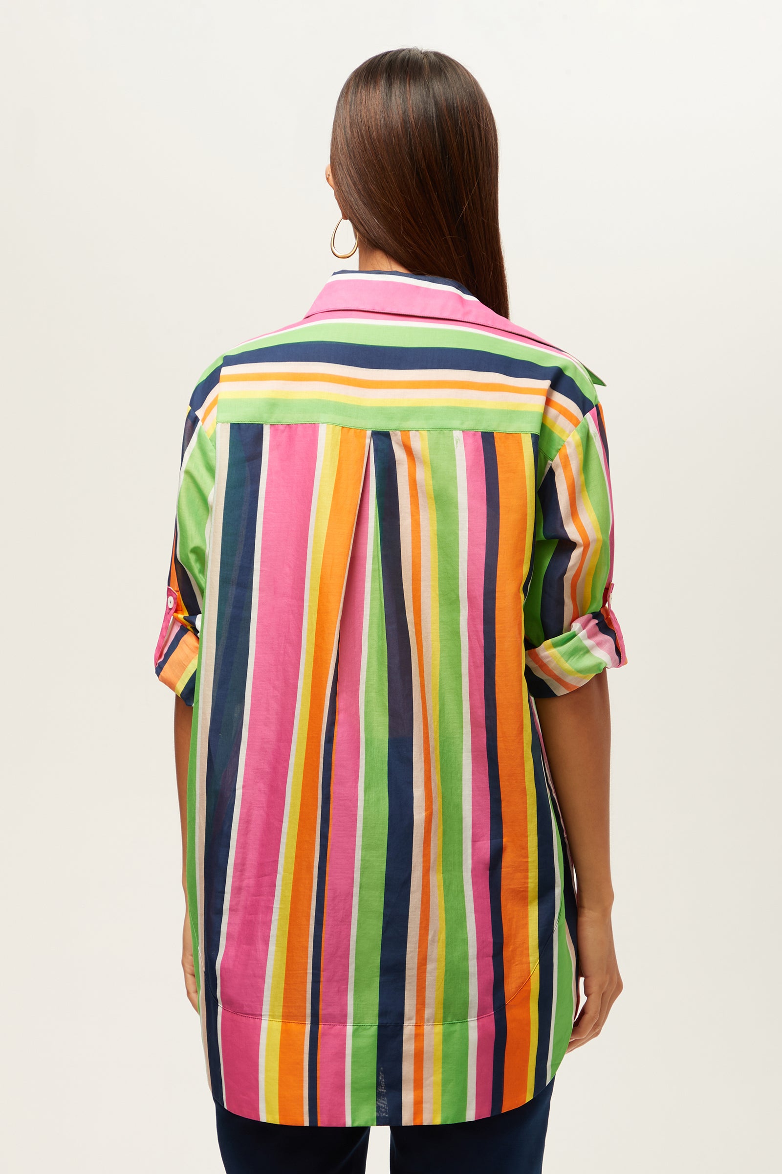 A person with long straight hair, wearing large hoop earrings and the Swing Short-Sleeve Top in Splash Stripe, stands facing away from the camera against a plain background.