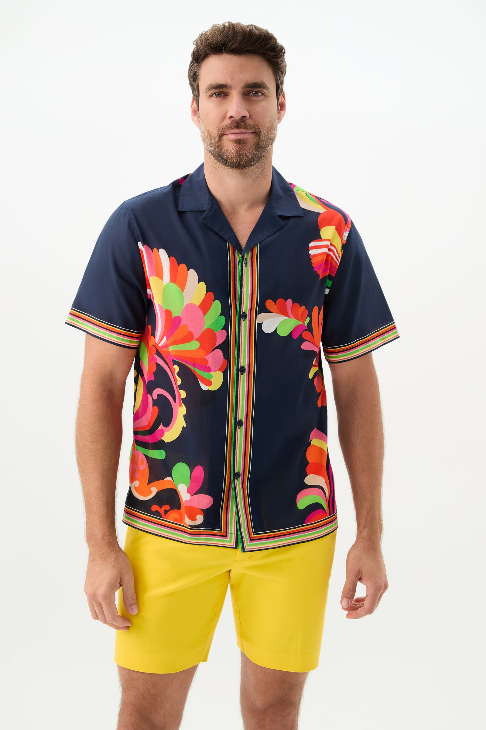 A man with short brown hair and a beard wears the Josue Short-Sleeve Shirt - Palms Paradise in Multi and yellow shorts, standing against a plain white background.
