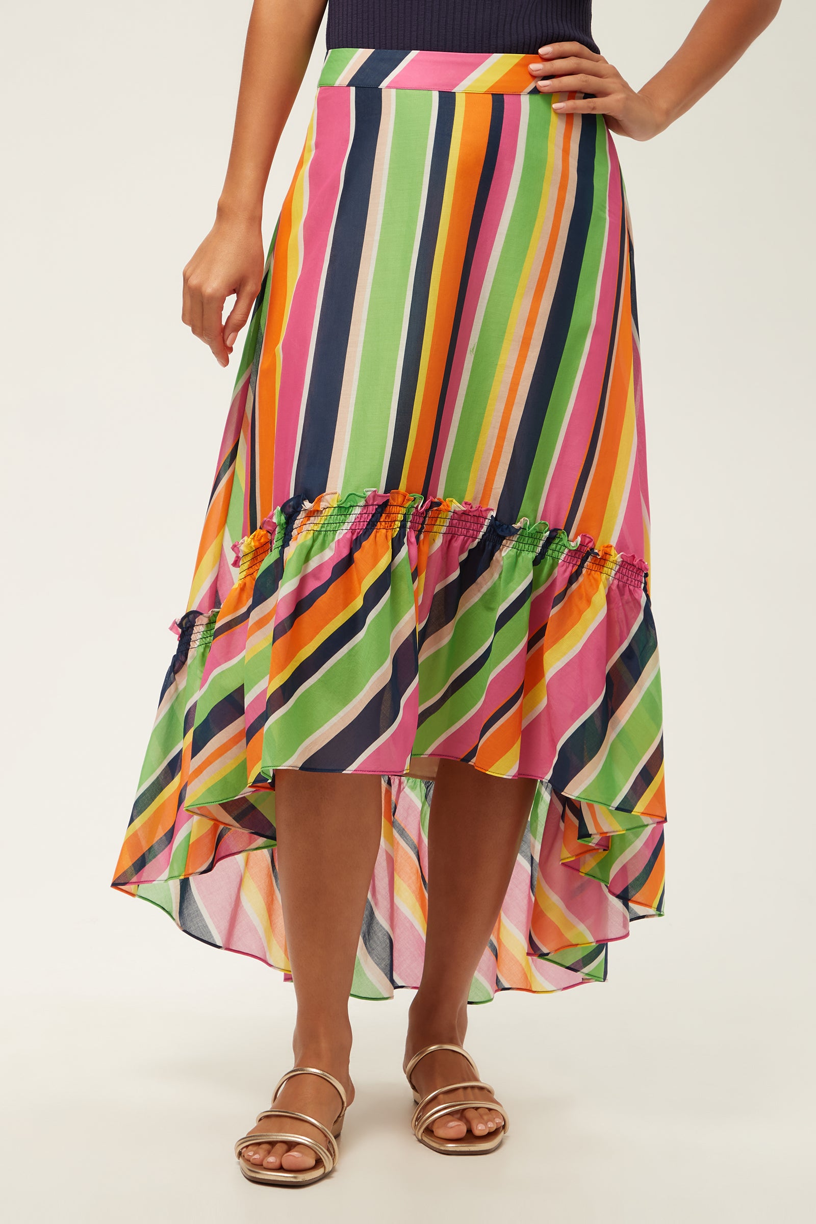 A person wears the Rosamund 2 High-Low Skirt - Splash Stripe in Multi, featuring diagonal stripes and ruffled detail, paired with gold sandals. The skirt is flowy and lightweight.