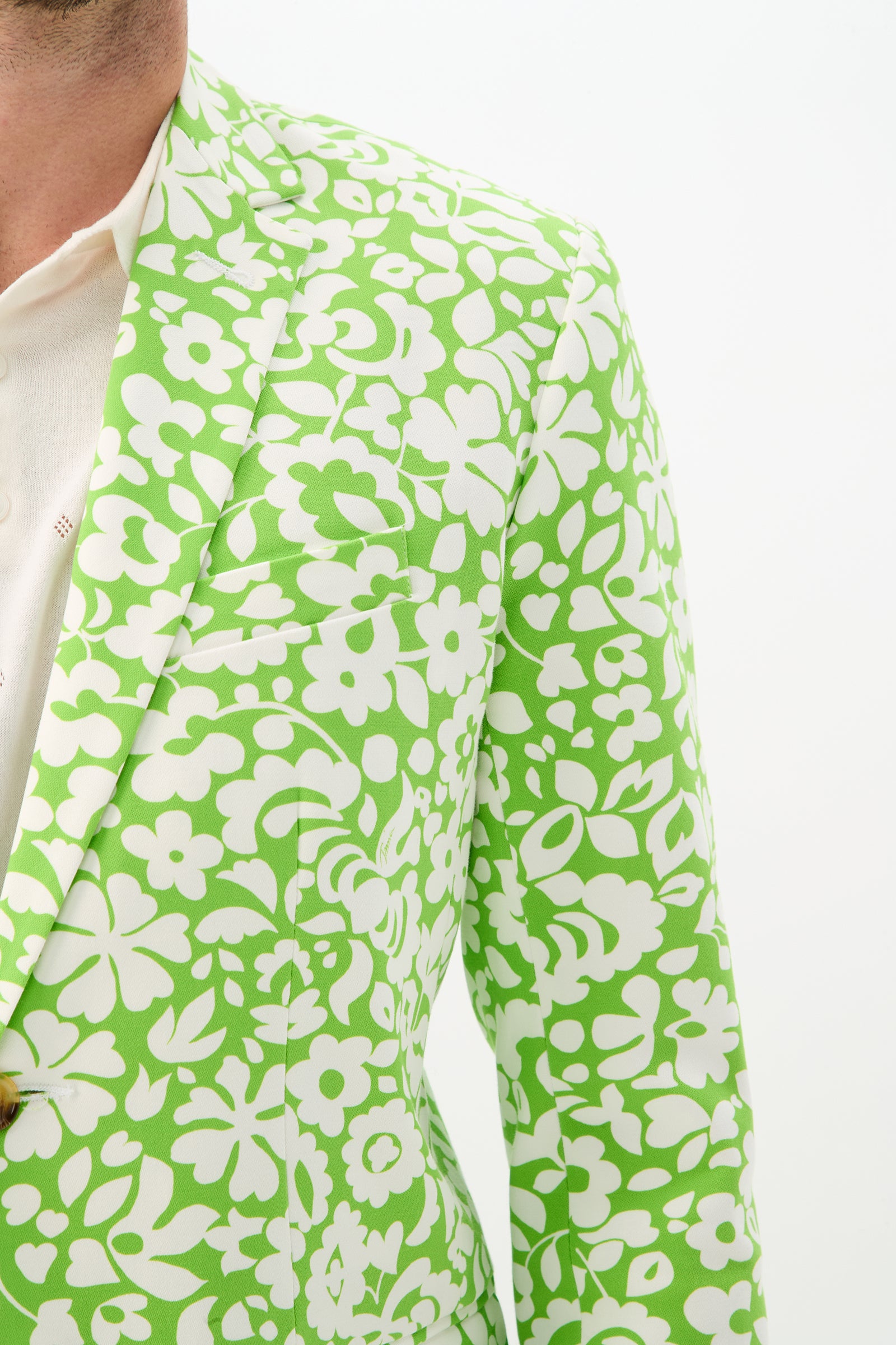 A person wearing the Thurston Blazer - Poolside Gossip, a bright green jacket with a bold white floral pattern over a cream shirt, is shown from shoulders to mid-torso against a plain white background.