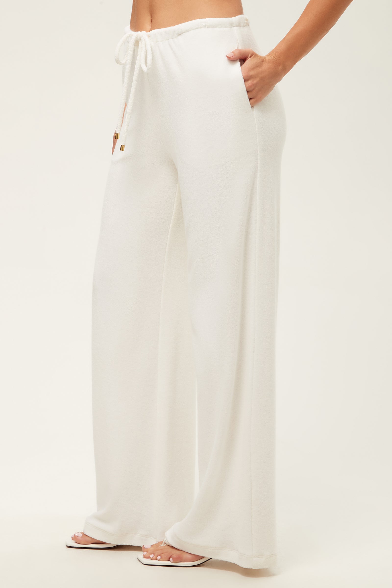 Someone is wearing the Linsk Wide-Leg Pant - Poolside Terry, featuring a loose fit, high waist, drawstring, and side pockets, paired with white open-toe sandals against a plain light background.