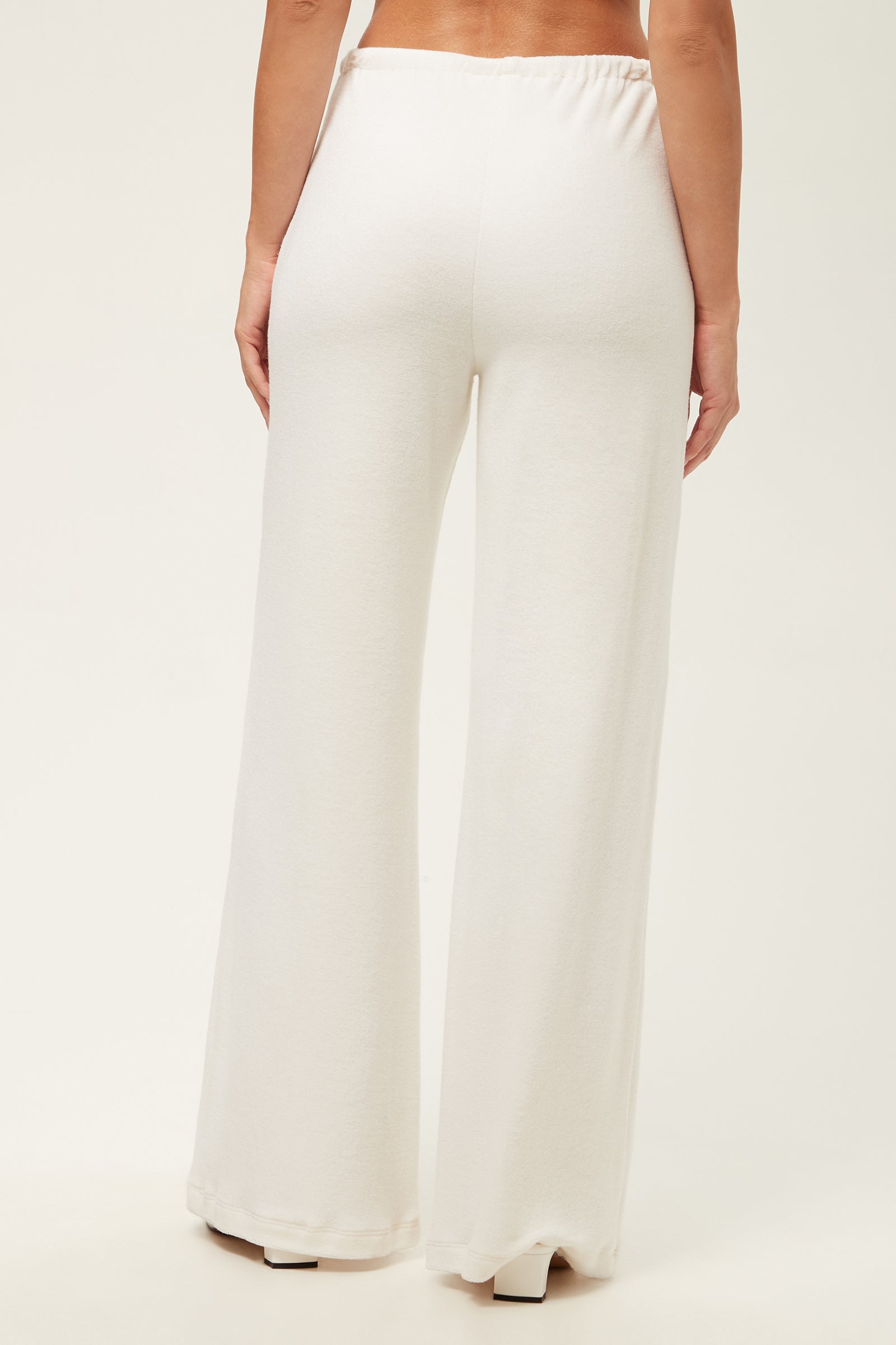 A person seen from the back stands against a plain light background, wearing the Linsk Wide-Leg Pant - Poolside Terry in white. These high-waisted pants feature a relaxed fit and an elastic waistband.