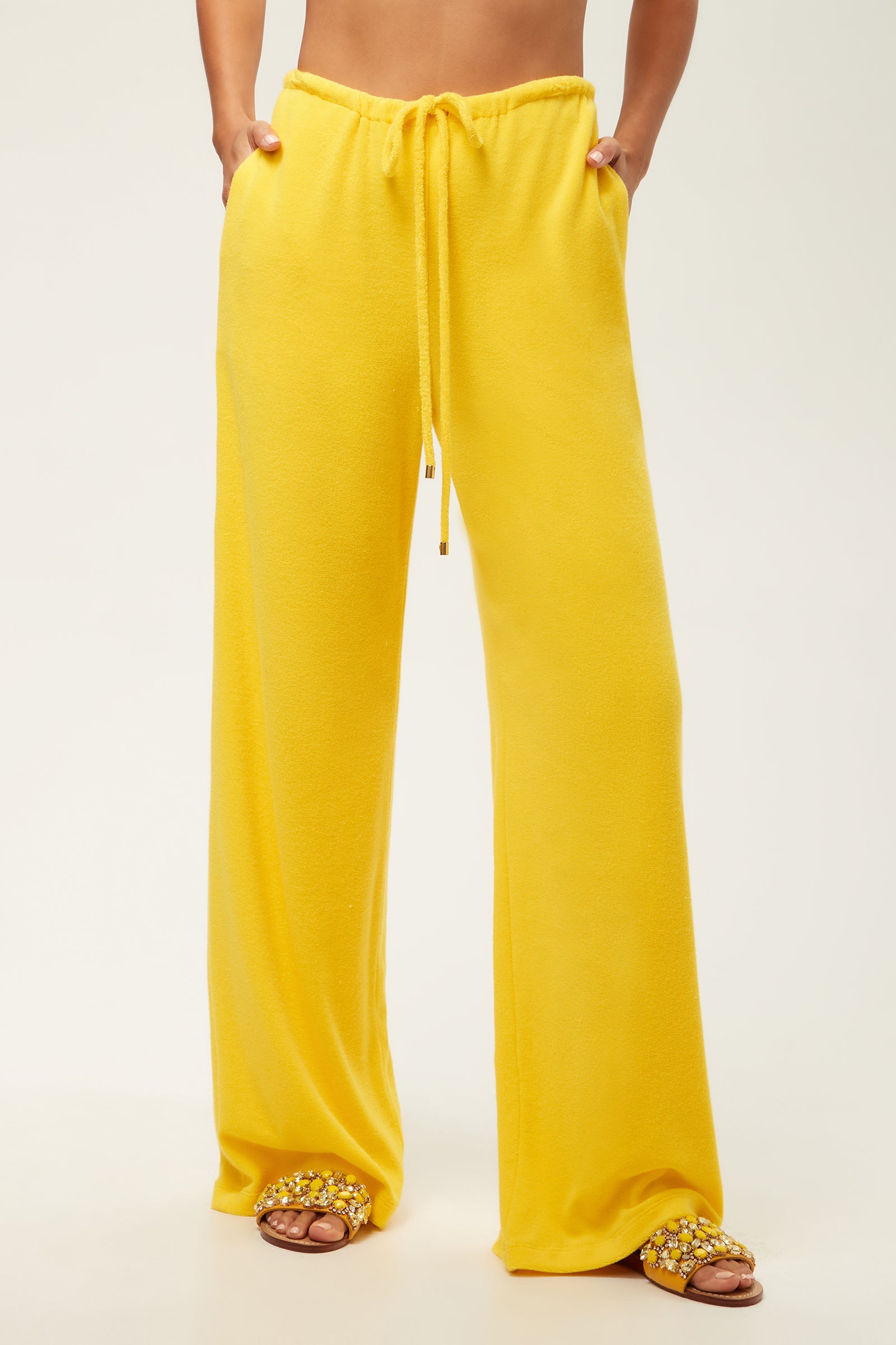 A person wearing the Linsk Wide-Leg Pant - Poolside Terry in Desert Sun and embellished slide sandals stands against a plain light background; only the lower half is visible.