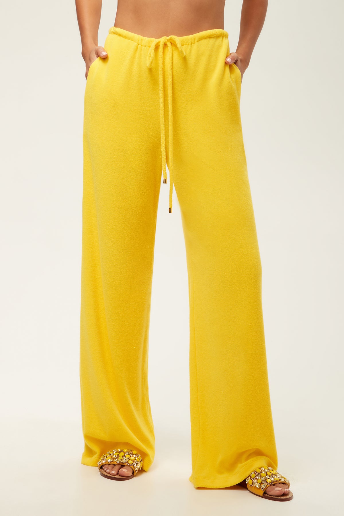 A person wearing the Linsk Wide-Leg Pant - Poolside Terry in Desert Sun and embellished slide sandals stands against a plain light background; only the lower half is visible.