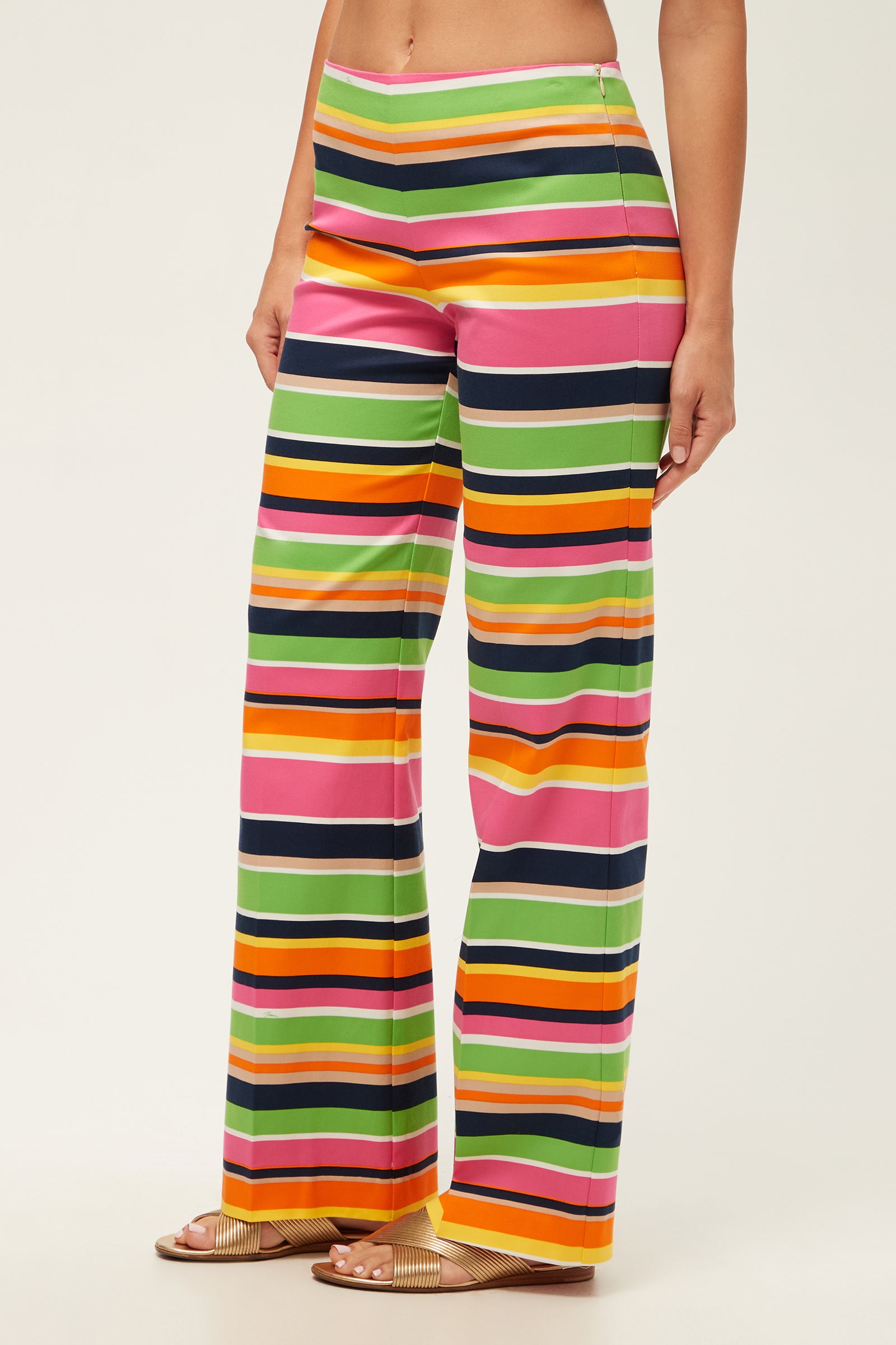 A person wearing the Rudi Straight-Leg Pant - Splash Stripe, featuring colorful horizontal stripes, paired with beige slide sandals.