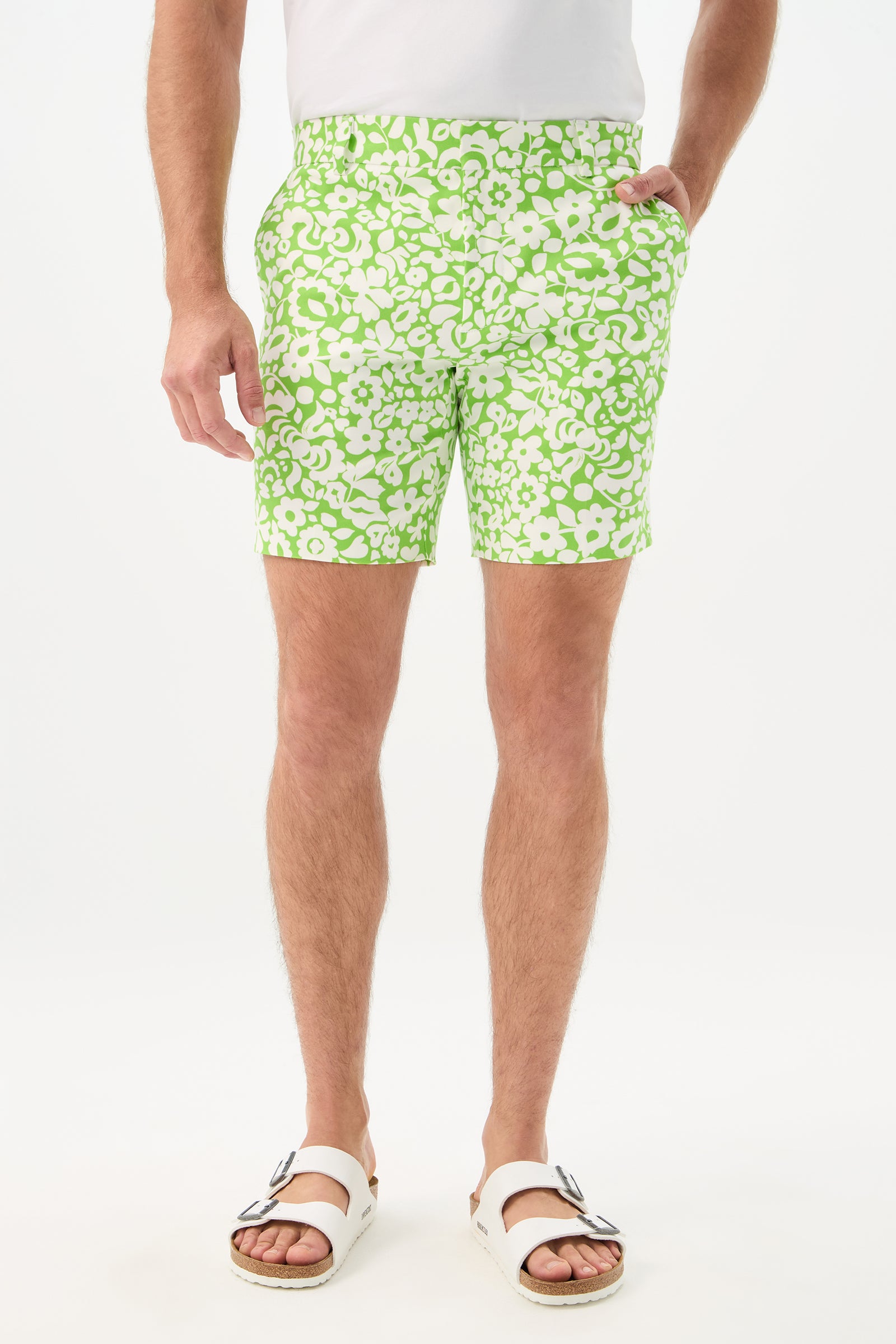 Wearing the Lawrence Short - Poolside Gossip in Serene Green, a person stands against a plain white background. They also wear a white shirt and sandals; the photo is cropped from the shoulders down.