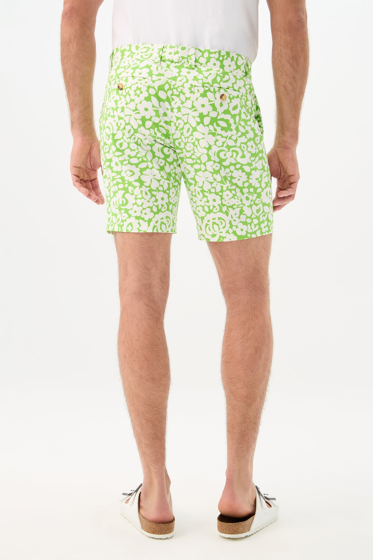 A man faces away, wearing the Lawrence Short - Poolside Gossip with a green and white floral print, paired with a white shirt and white slip-on shoes with brown soles, set against a plain white background.