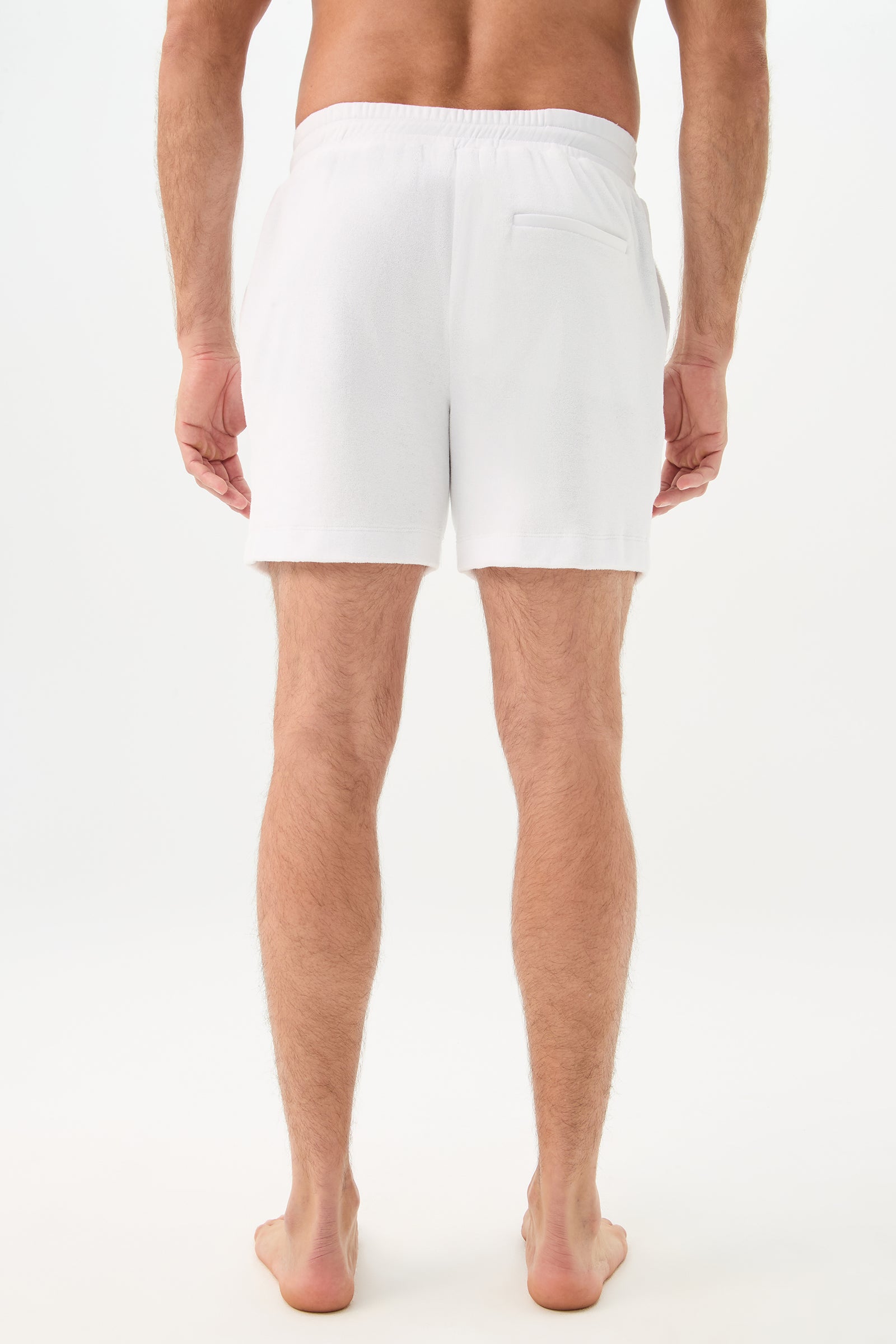 A person stands barefoot on a white surface, shown from behind, wearing the Lounge Knit Short - Linsk Terry featuring an elastic waistband and single back pocket. The background is plain white.
