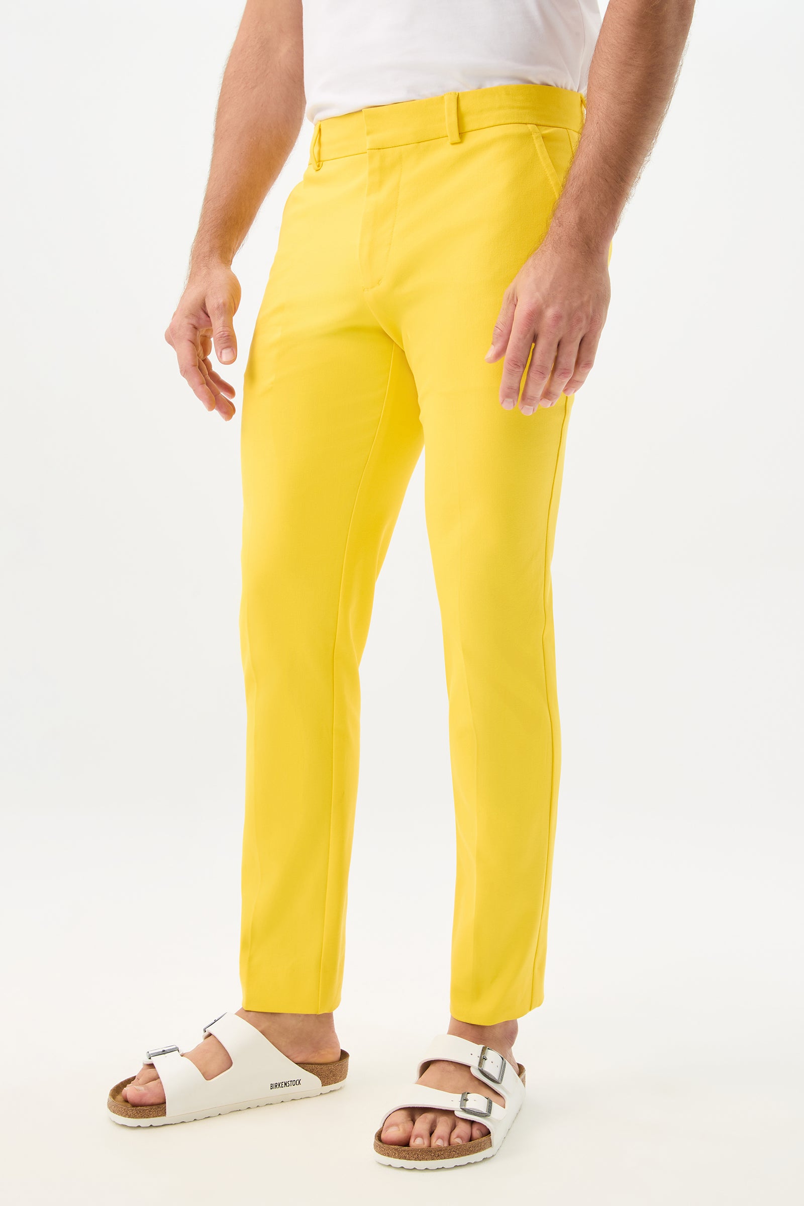 A person wears the Clyde Slim Trouser - Sunset Stretch and white Birkenstock sandals, standing against a plain white background with only their lower half visible.