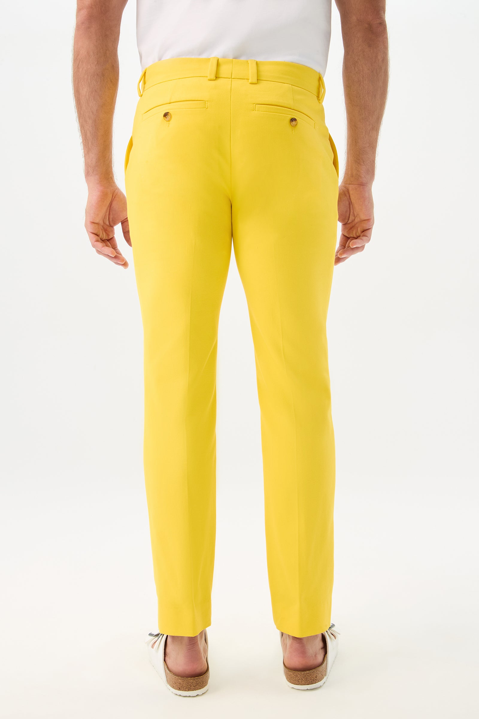 A person stands with their back to the camera against a plain white background, wearing Clyde Slim Trouser - Sunset Stretch and light-colored shoes.