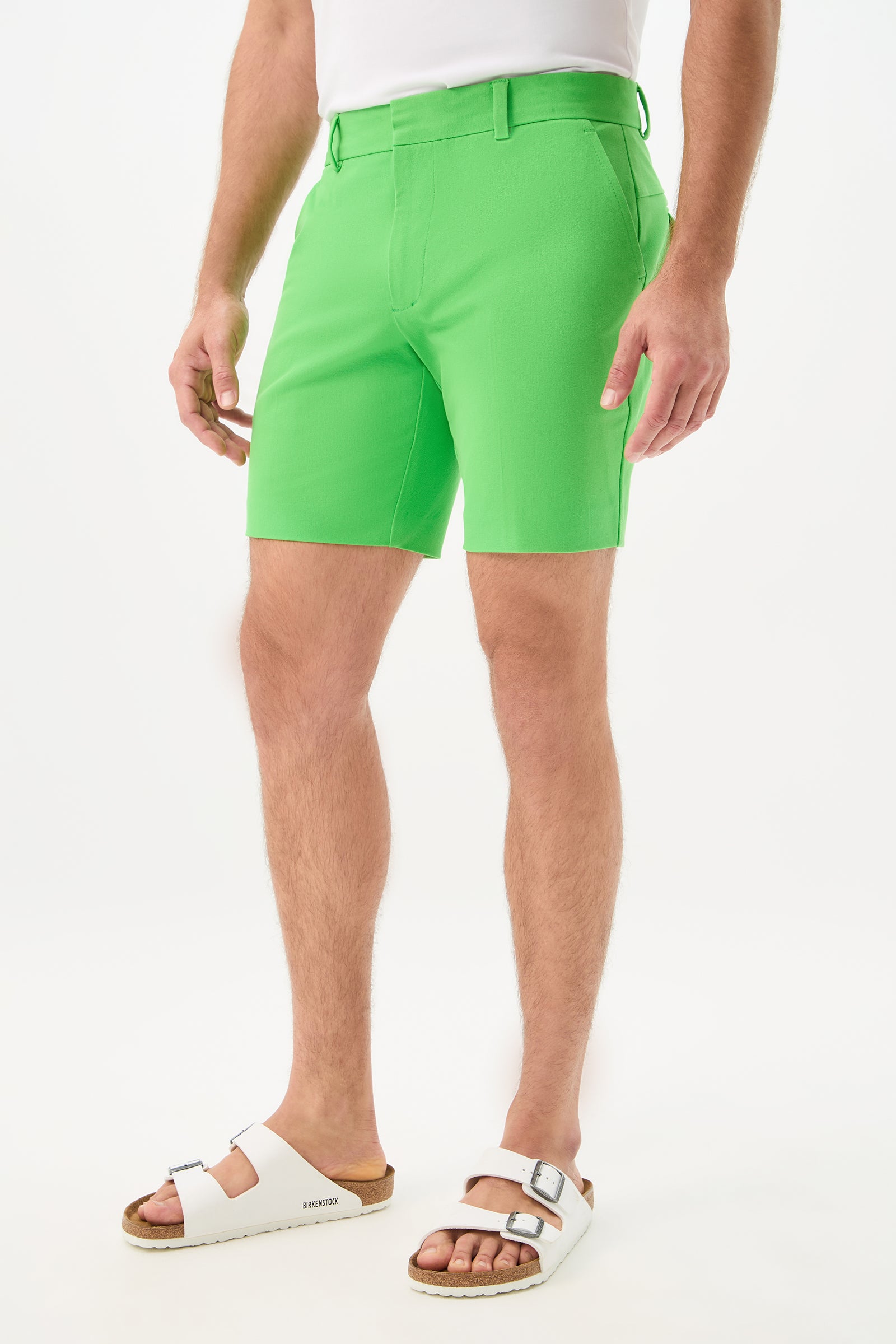 A person models the Cyrus Short - Cotton Bi-Stretch in bright green with white Birkenstock sandals, standing against a plain white background. Only their lower half is visible.