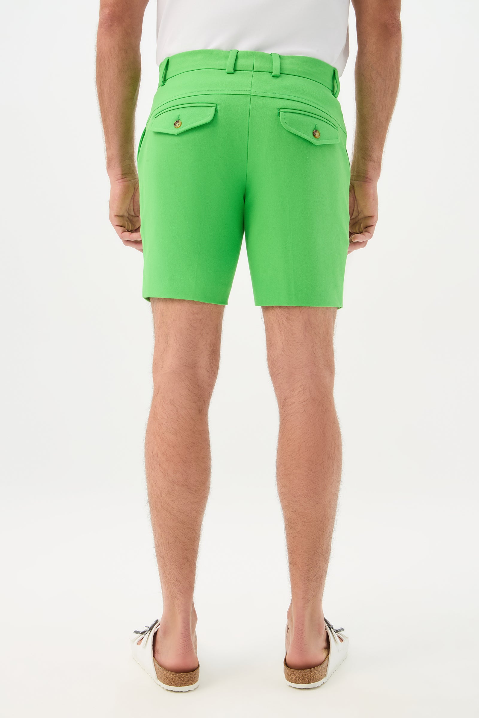 Someone wearing the Cyrus Short - Cotton Bi-Stretch in bright green, paired with a white shirt and white slip-on shoes, stands with their back to the camera against a plain white background.