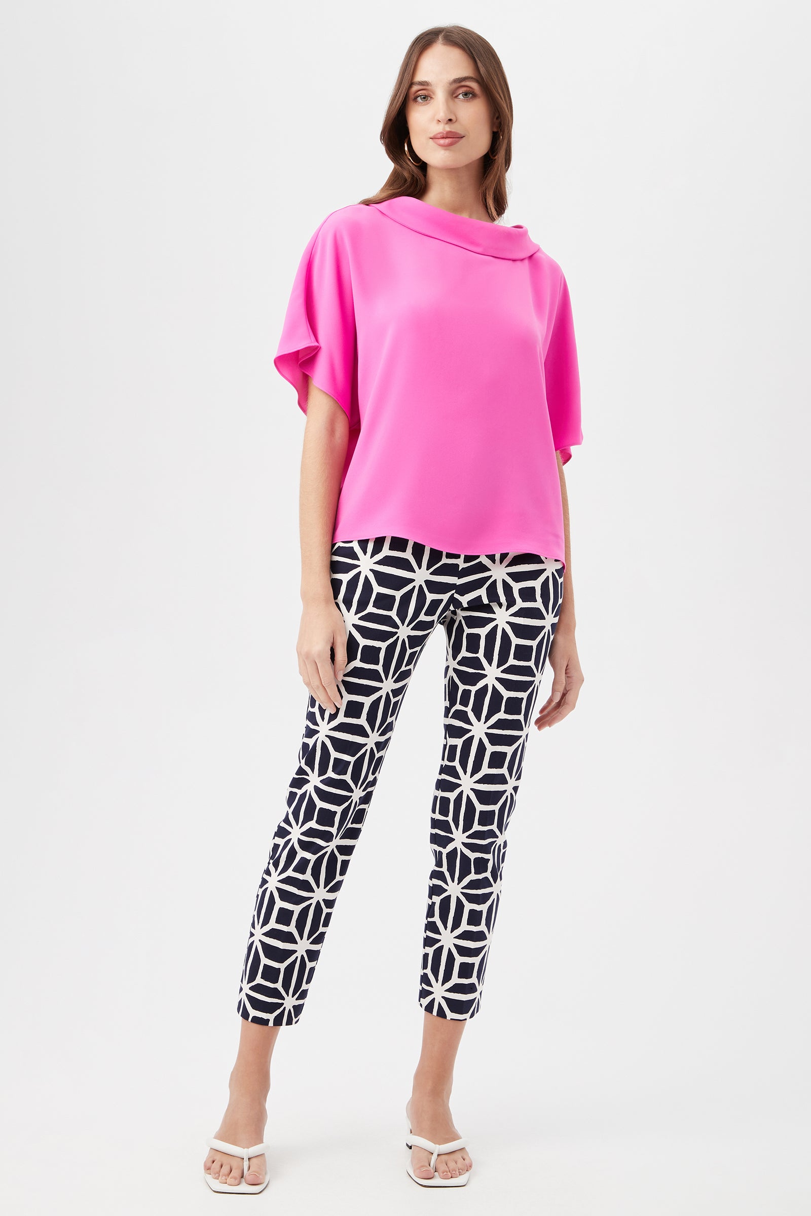 A woman models the Honeysuckle Boatneck Dolman-Sleeve Top in bright pink, along with navy-and-white geometric pants and white heeled sandals, standing against a plain white background.