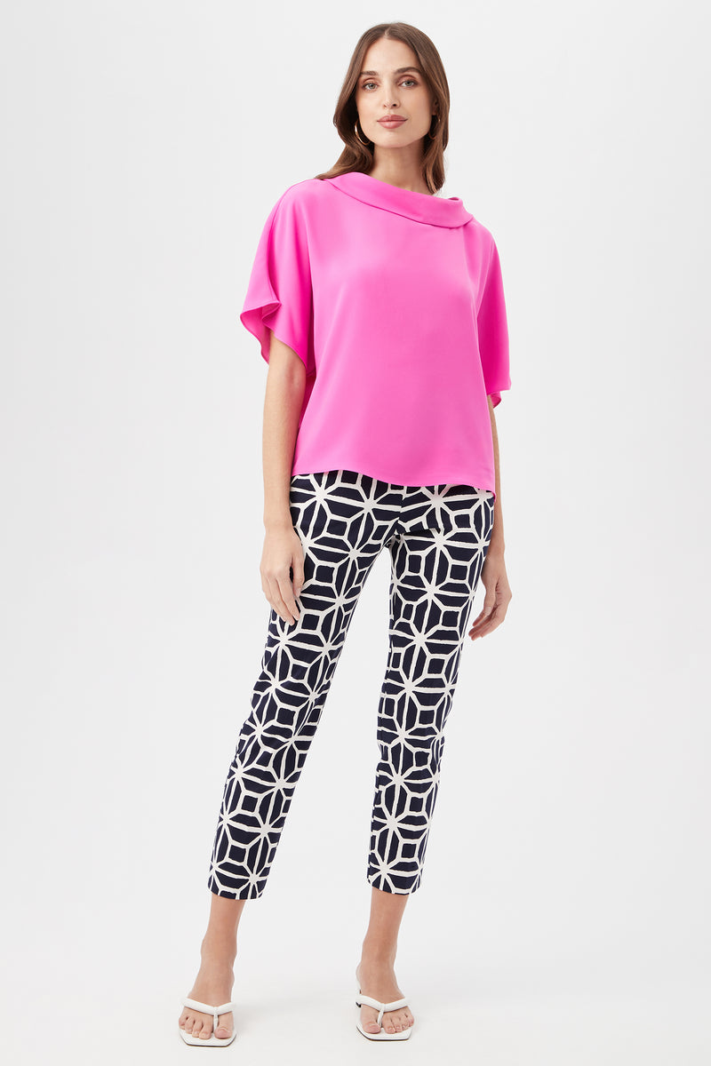 A woman models the Honeysuckle Boatneck Dolman-Sleeve Top in bright pink, along with navy-and-white geometric pants and white heeled sandals, standing against a plain white background.