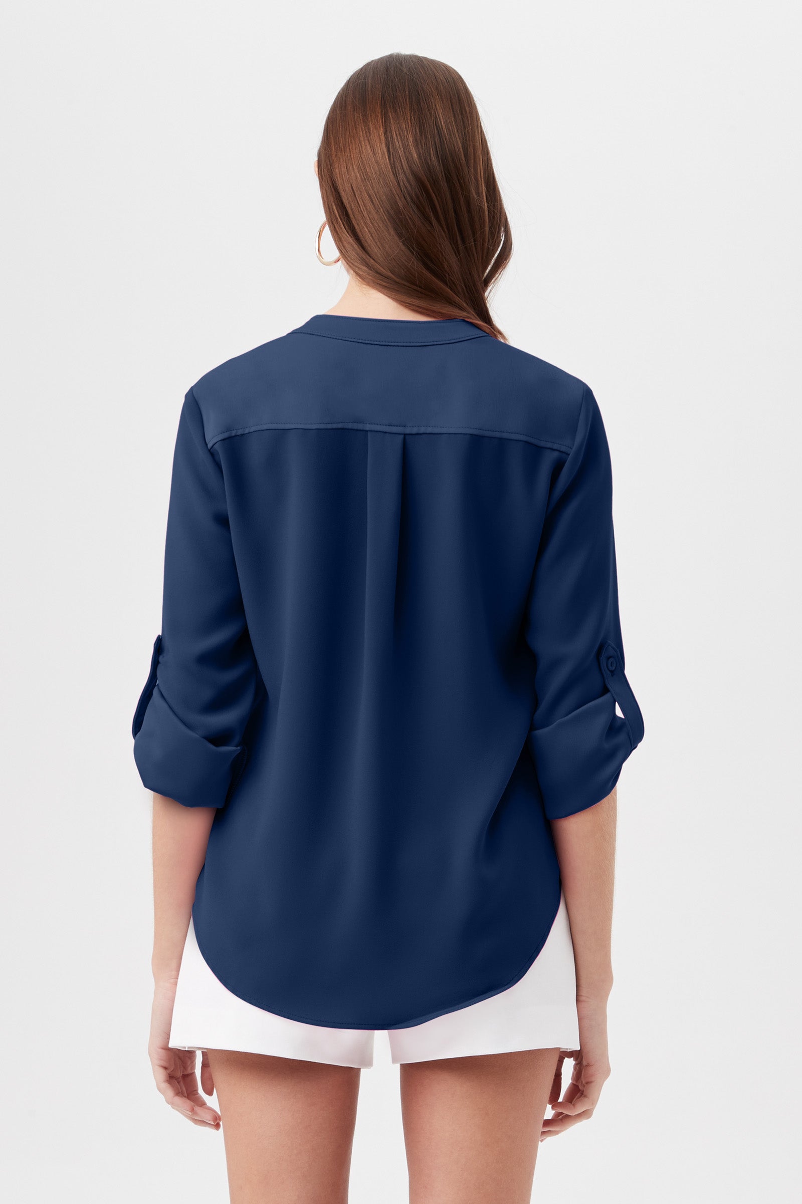 A woman with long brown hair stands facing away, wearing the Kaiko 3/4-Sleeve Half-Zip Top in navy and white shorts against a plain white background.