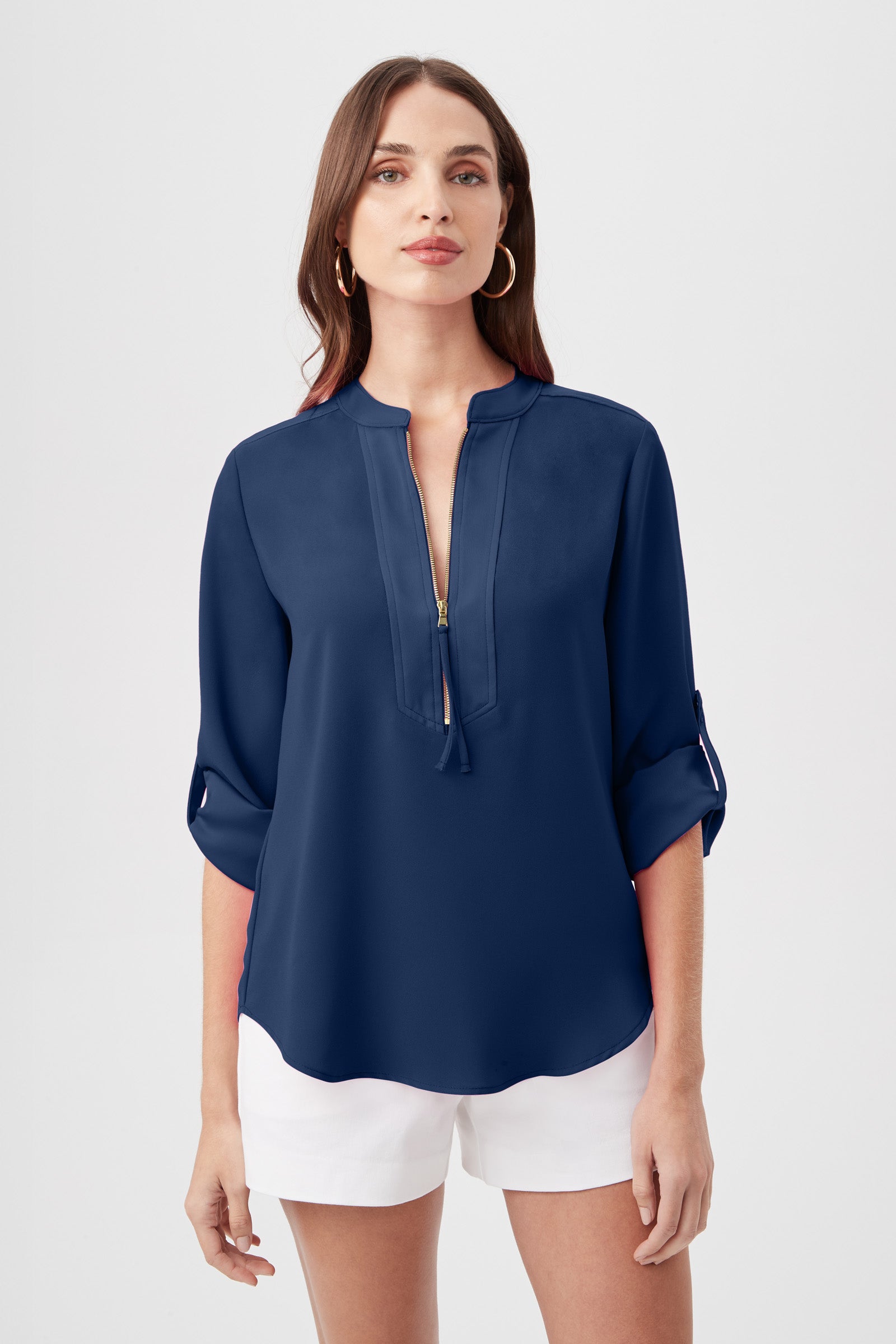 A woman with straight brown hair and gold hoop earrings wears the Kaiko 3/4-Sleeve Half-Zip Top in navy blue and white shorts, facing forward with a neutral expression.