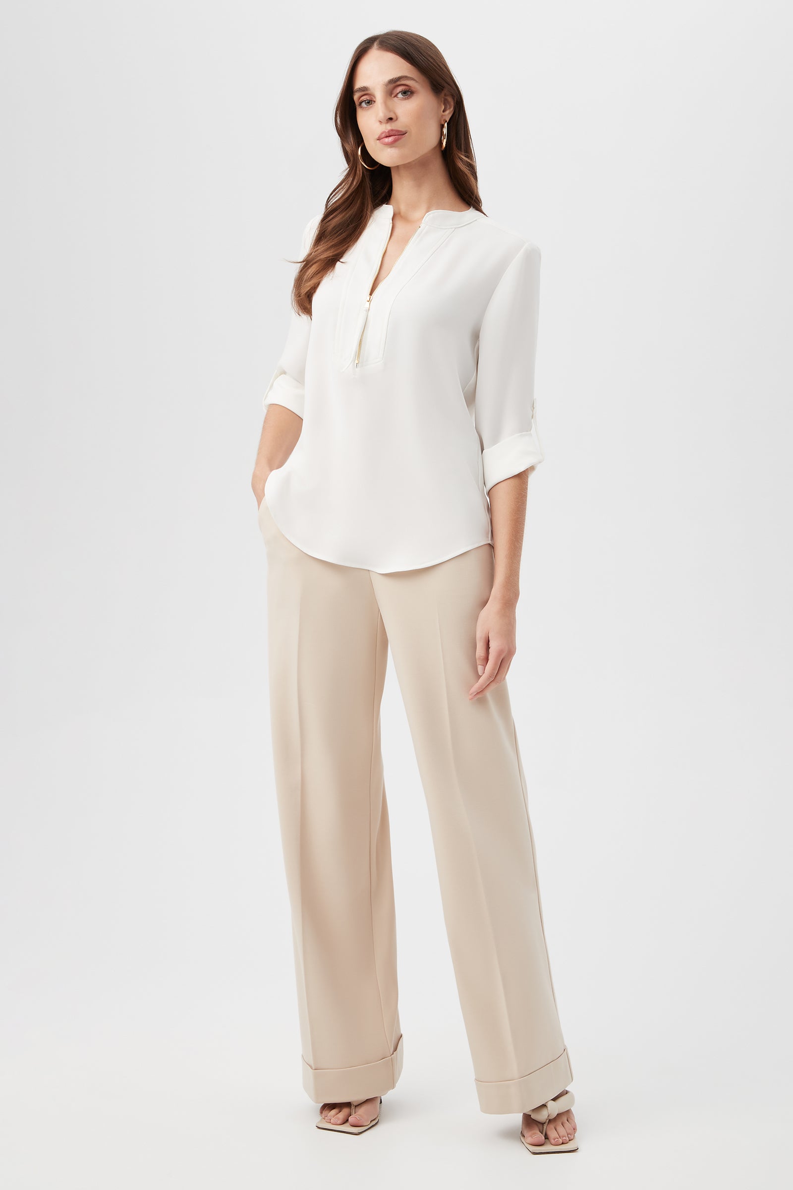 A woman stands confidently in the Kaiko 3/4-Sleeve Half-Zip Top and beige wide-leg trousers, paired with high-heeled sandals. Her long hair is loose, and she maintains a neutral expression against a plain white background.