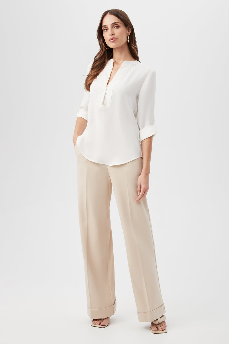 A woman stands confidently in the Kaiko 3/4-Sleeve Half-Zip Top and beige wide-leg trousers, paired with high-heeled sandals. Her long hair is loose, and she maintains a neutral expression against a plain white background.