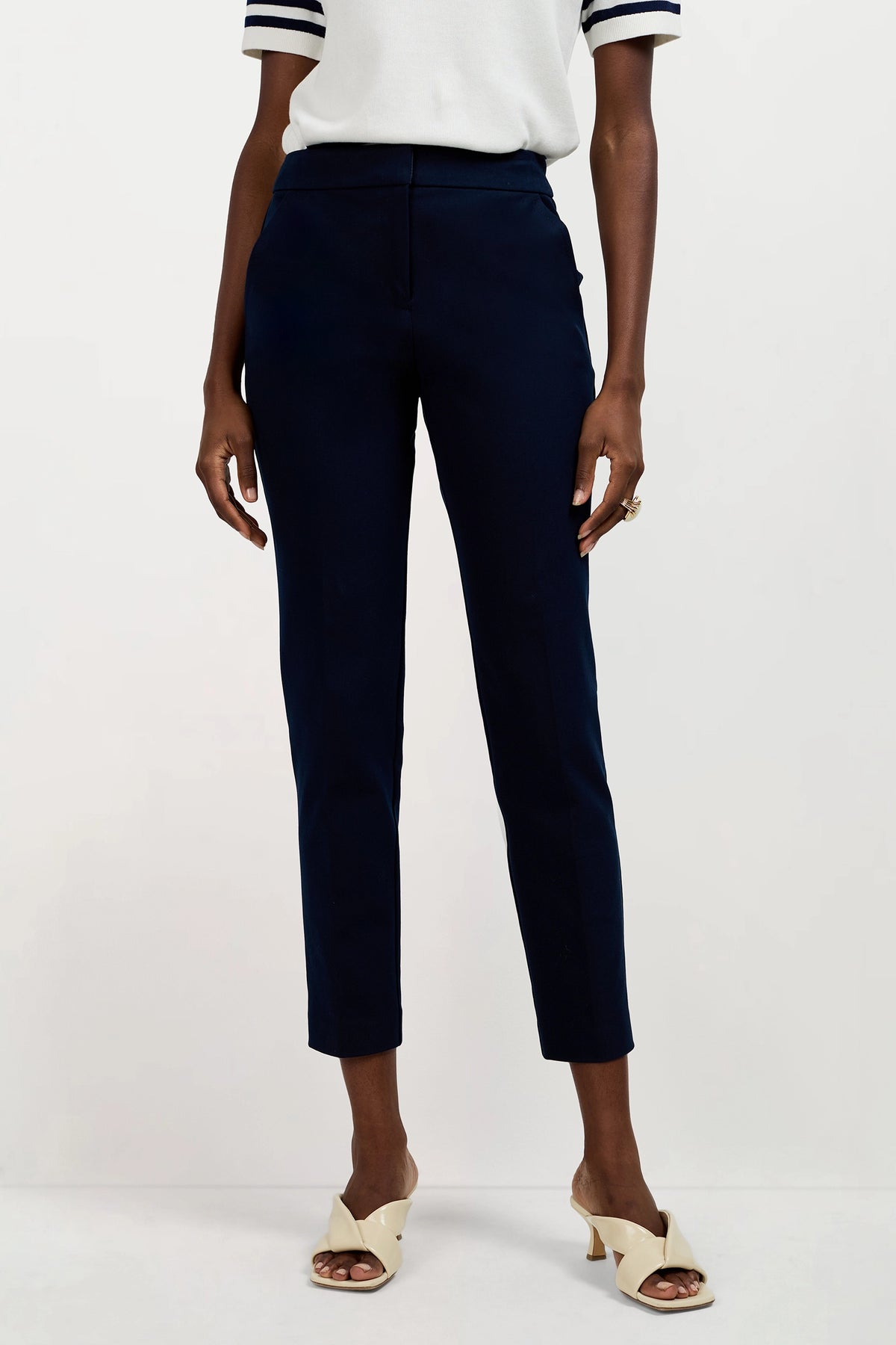 Wearing Aubree 2 Cigarette Pants in dark navy, a short-sleeved white top with dark striped cuffs, and cream open-toe heeled sandals, a person stands against a plain light background.